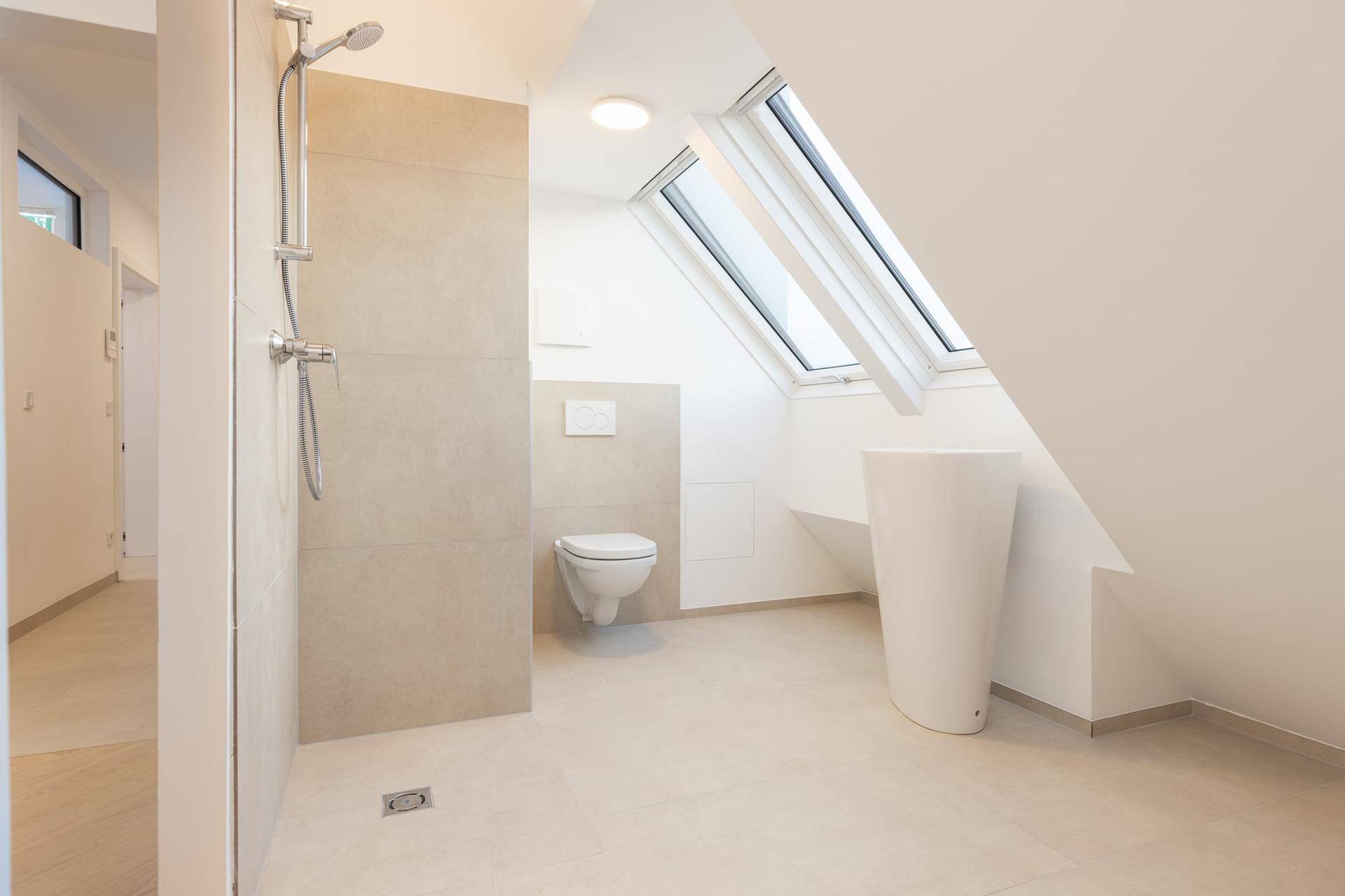 Modernes Badezimmer mit begehbarer Dusche, wandhängendem WC und hellen Dachfenstern.