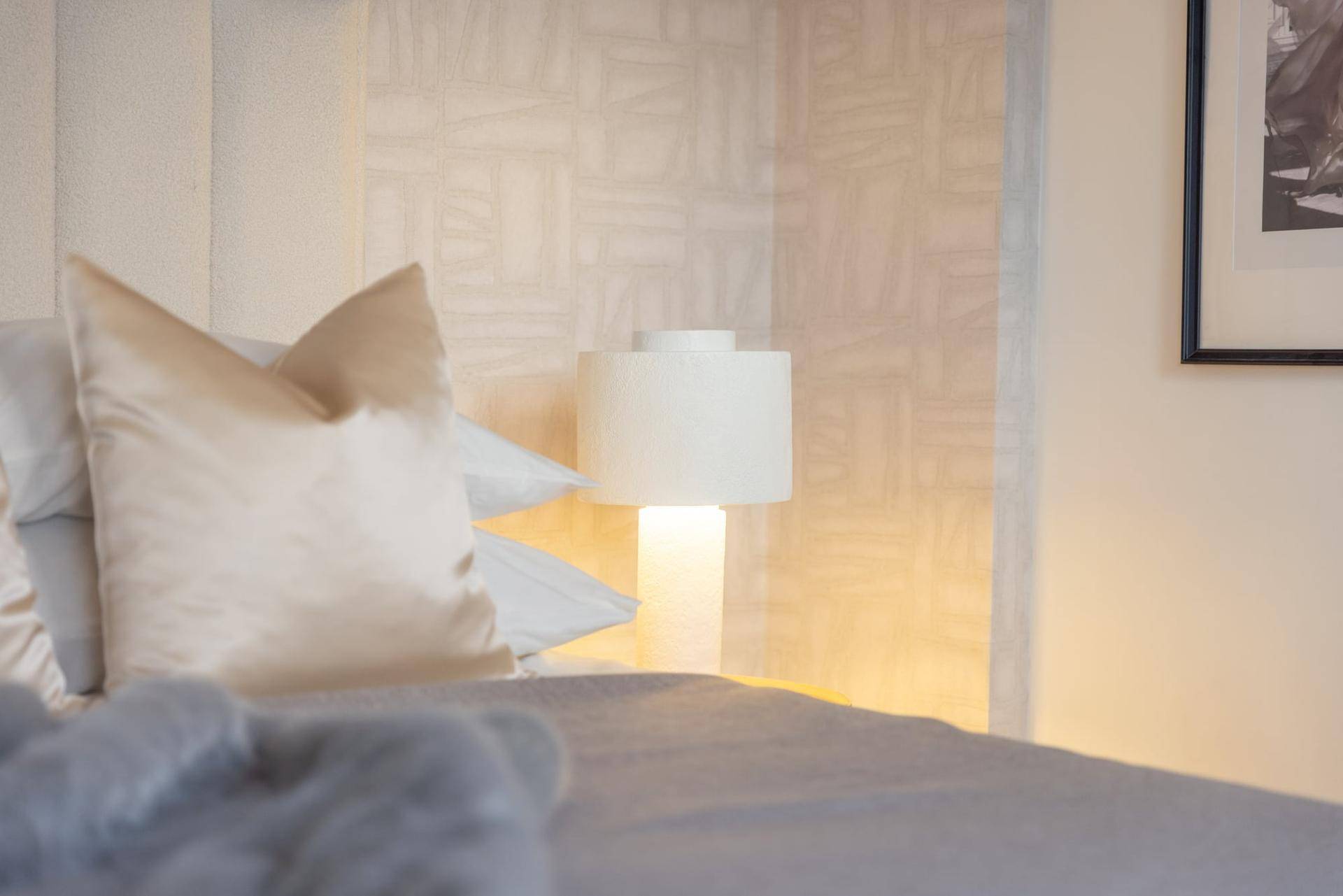 Nahaufnahme eines gemütlichen Schlafzimmers mit weichen Kissen und einer modernen Nachttischlampe.