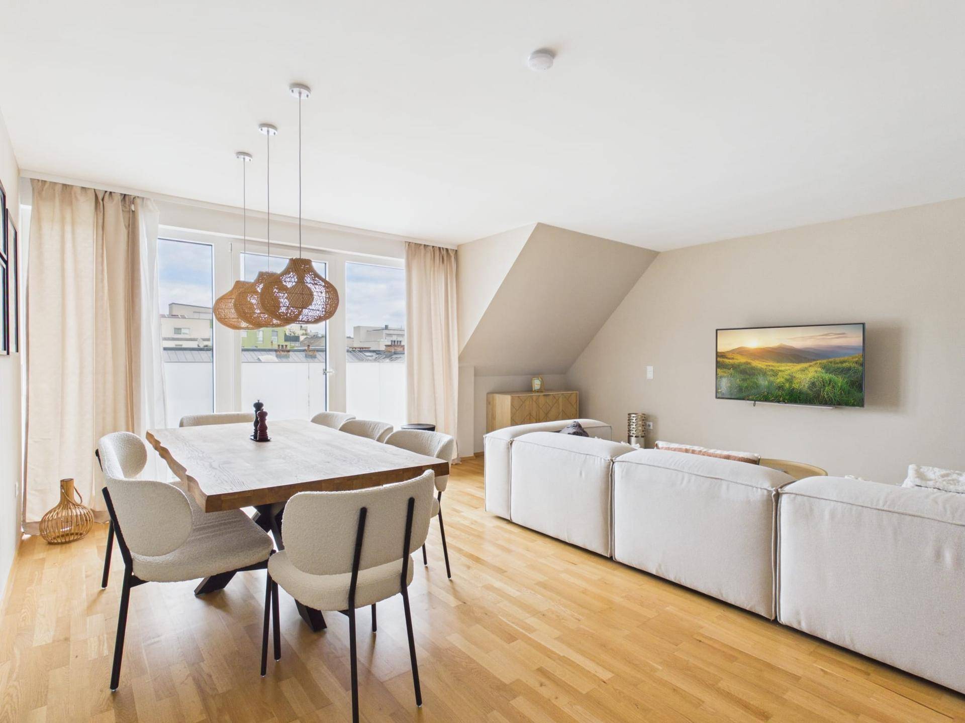 Heller Wohn- und Essbereich mit Holzboden, großem Esstisch und gemütlichem Sofa.