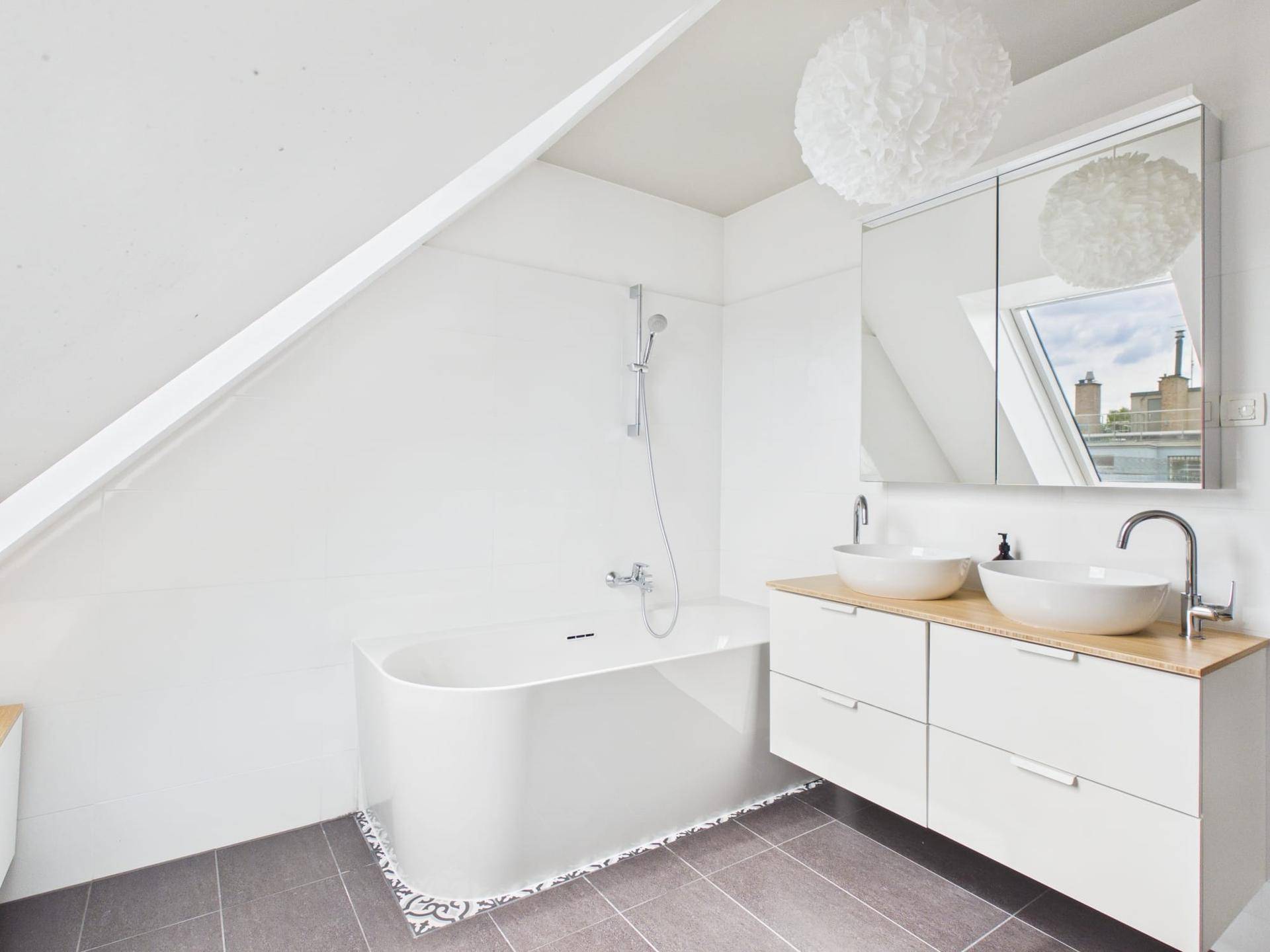 Helles Badezimmer mit Badewanne, Doppelwaschbecken und Spiegelschrank unter Dachschräge.