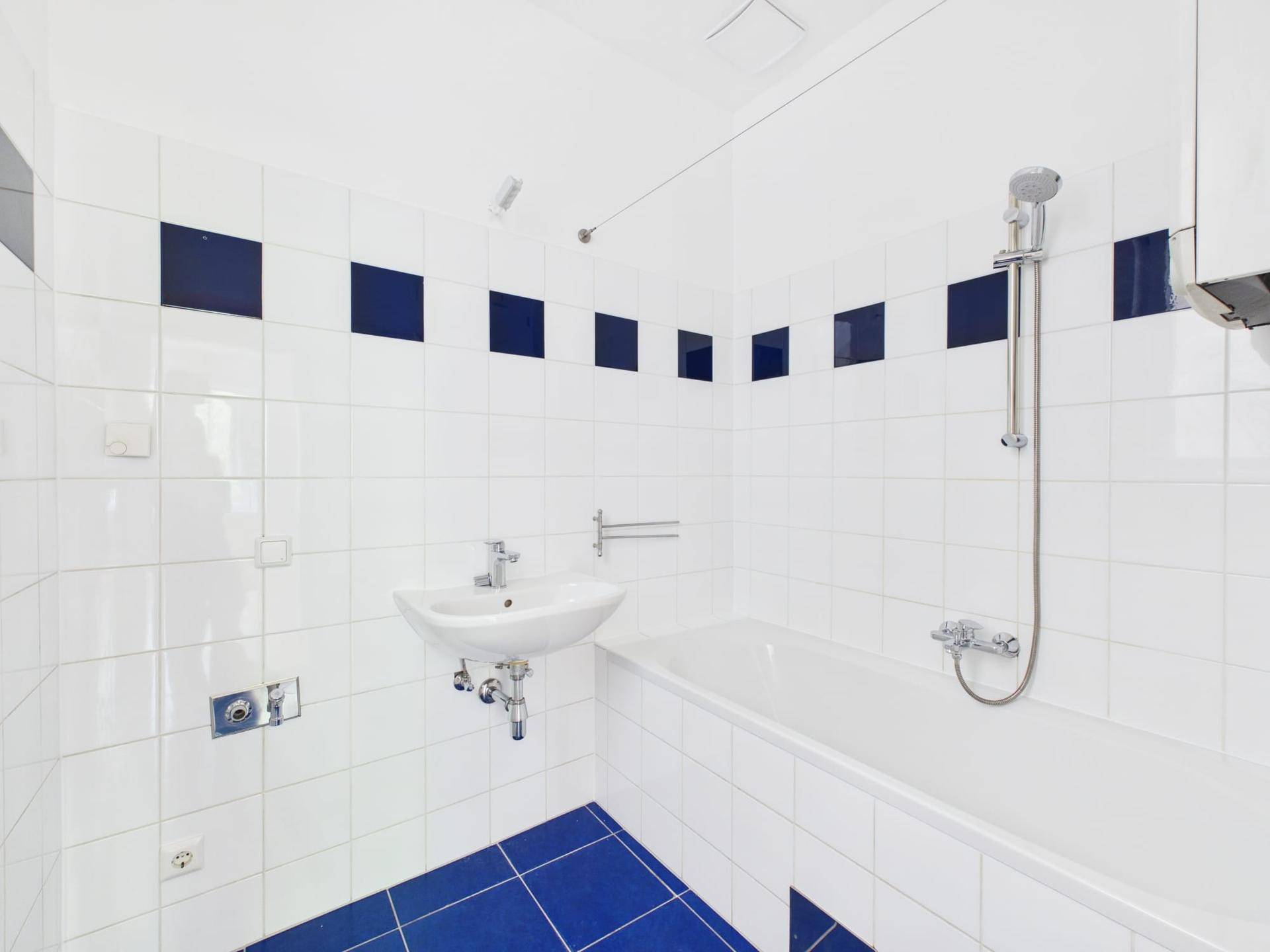 Badezimmer mit weißen und blauen Fliesen, Waschbecken und Badewanne mit Duschfunktion.