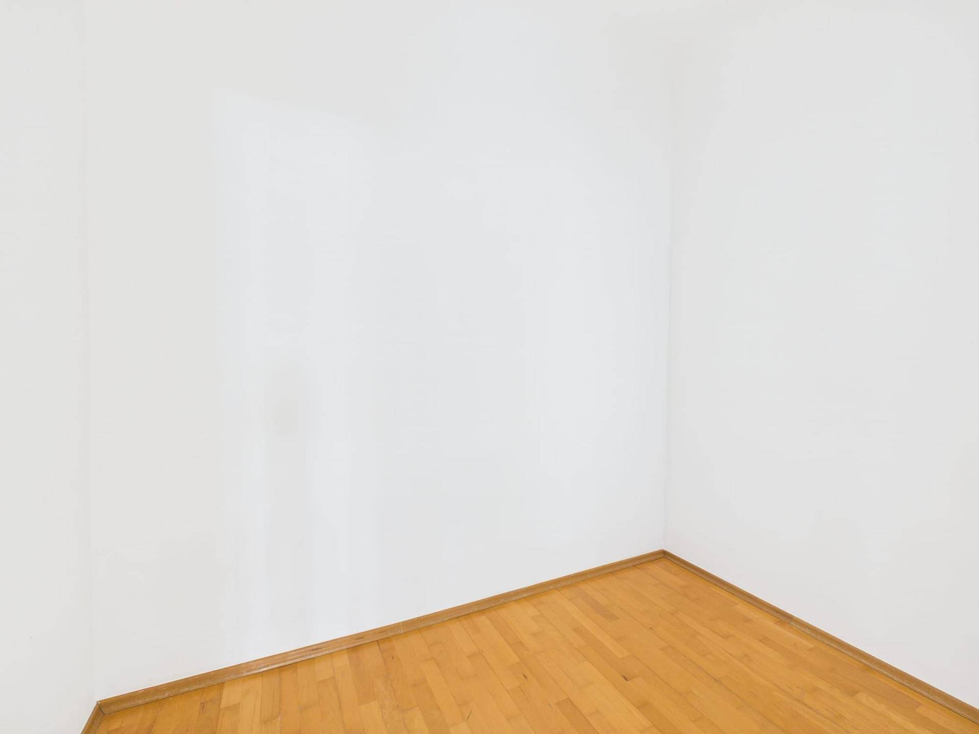 Ecke eines leeren Zimmers mit hellem Holzplankenboden und weißen Wänden.