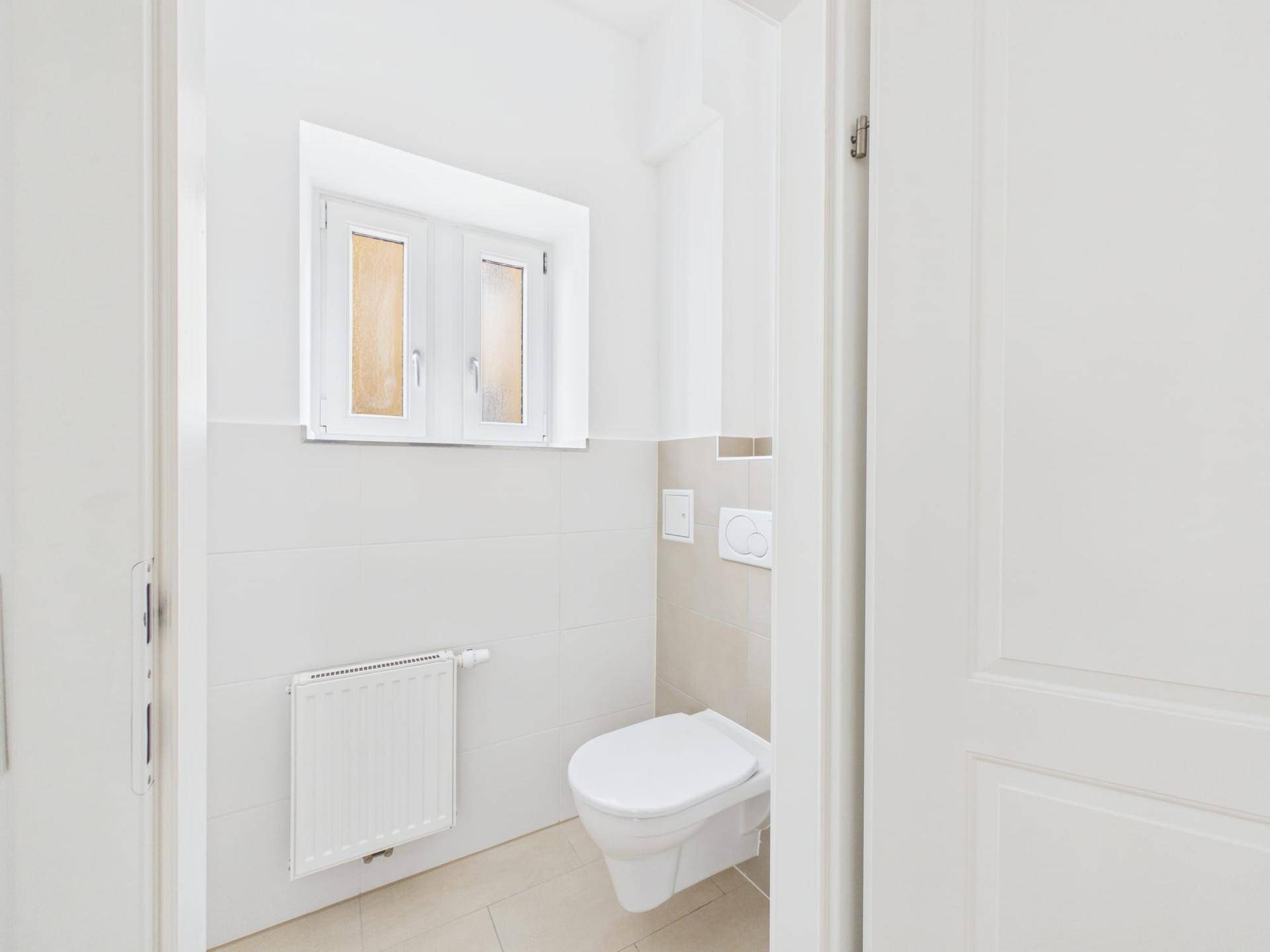 Kleines Gäste-WC mit wandhängender Toilette, Heizkörper und einem Fenster für Belüftung.