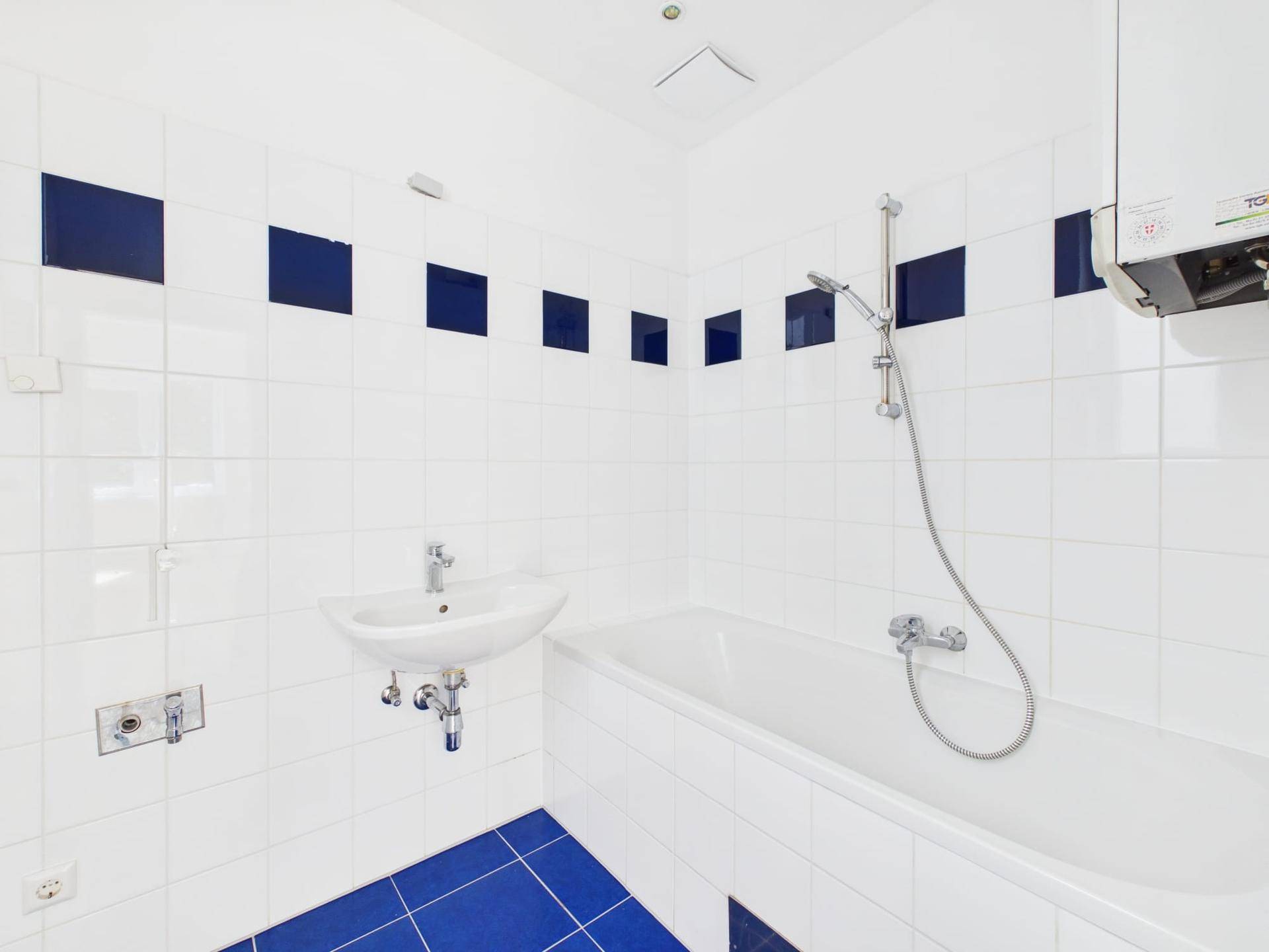 Badezimmer mit weiß-blauen Fliesen, Badewanne und Waschbecken in gutem Zustand.