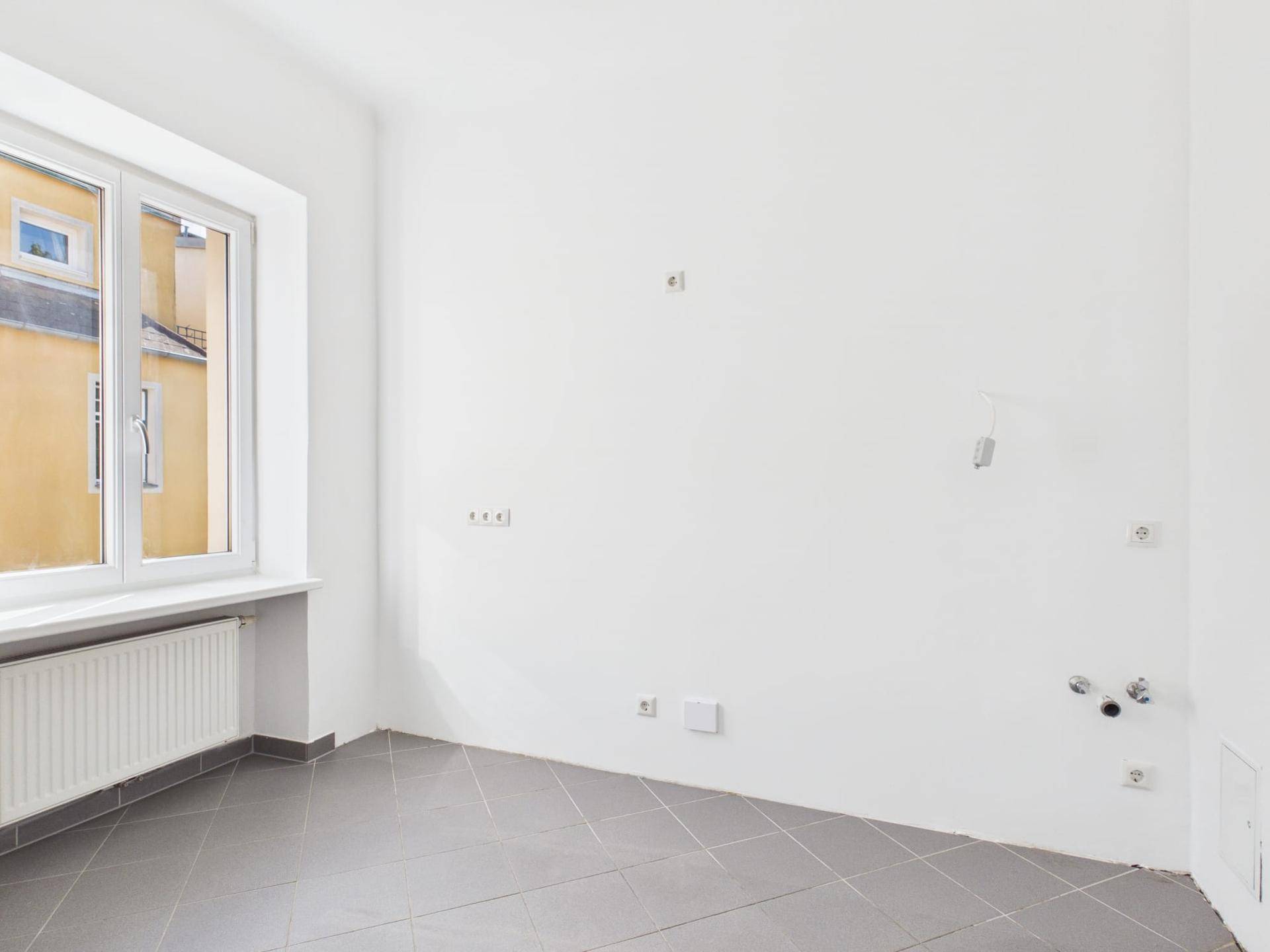 Leerer Küchenraum mit Fliesenboden und Anschlüssen für eine zukünftige Einbauküche.