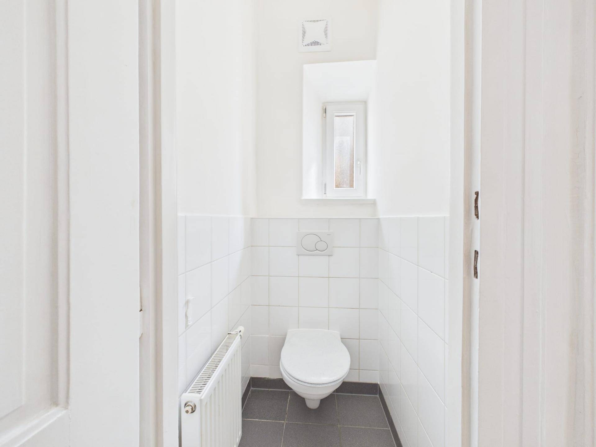 Kleines Gäste-WC mit Wand-WC, weißen Fliesen und einem kleinen Fenster.