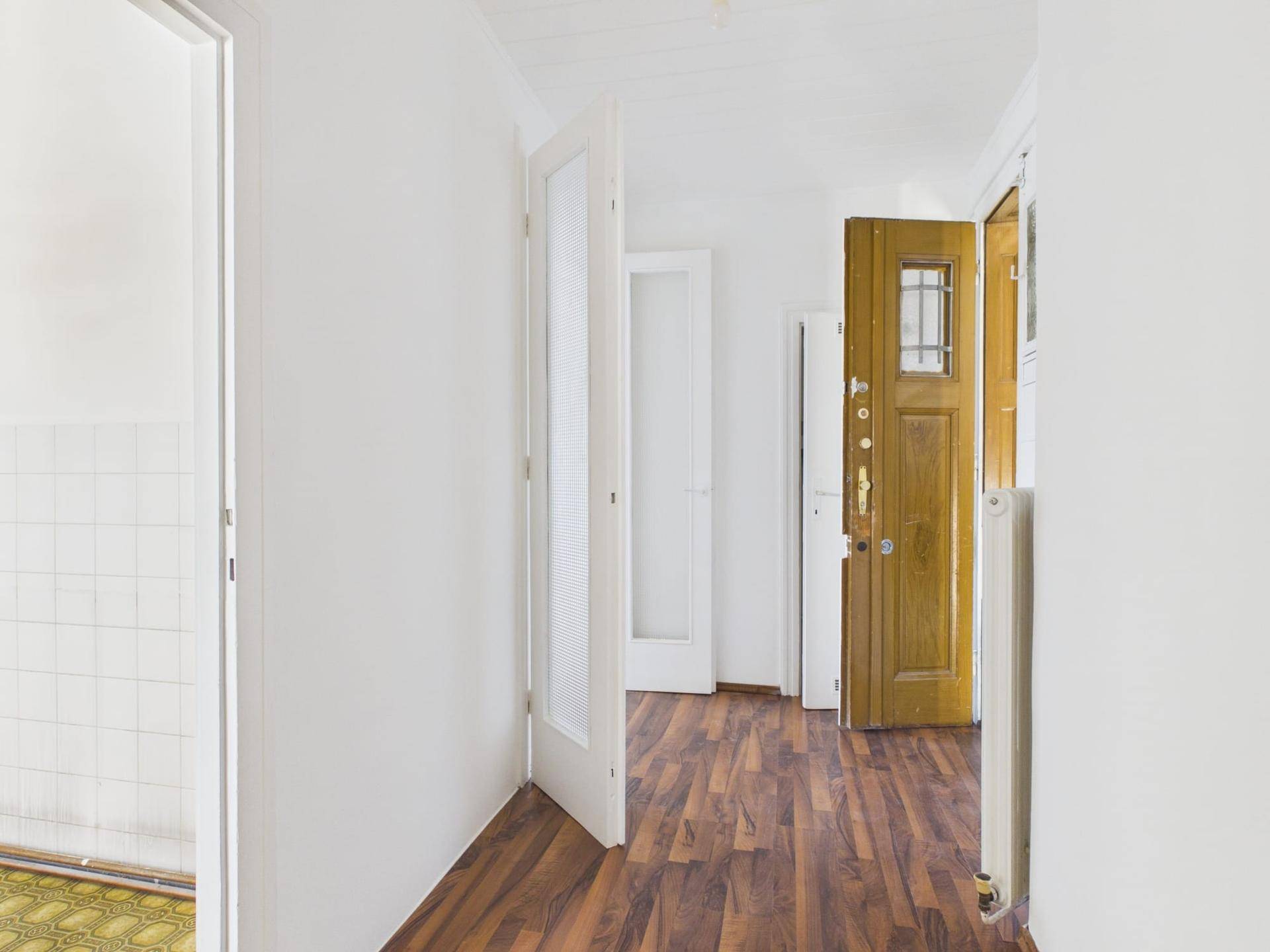 Langer Flur mit dunklem Laminatboden und mehreren Holztüren, die zu verschiedenen Räumen führen.