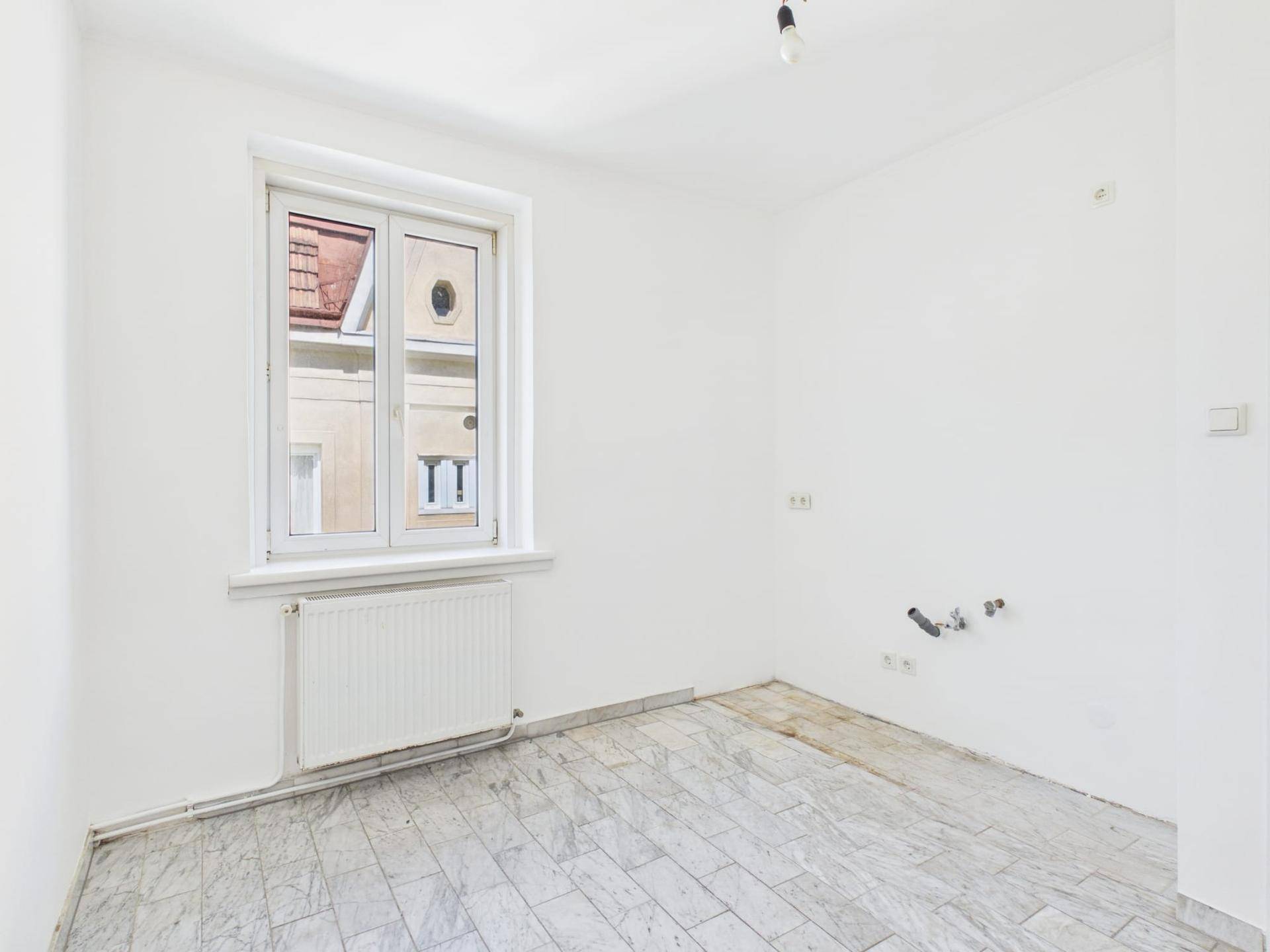 Leere Küche mit Fliesenboden und Fenster, bereit für die Installation neuer Geräte.