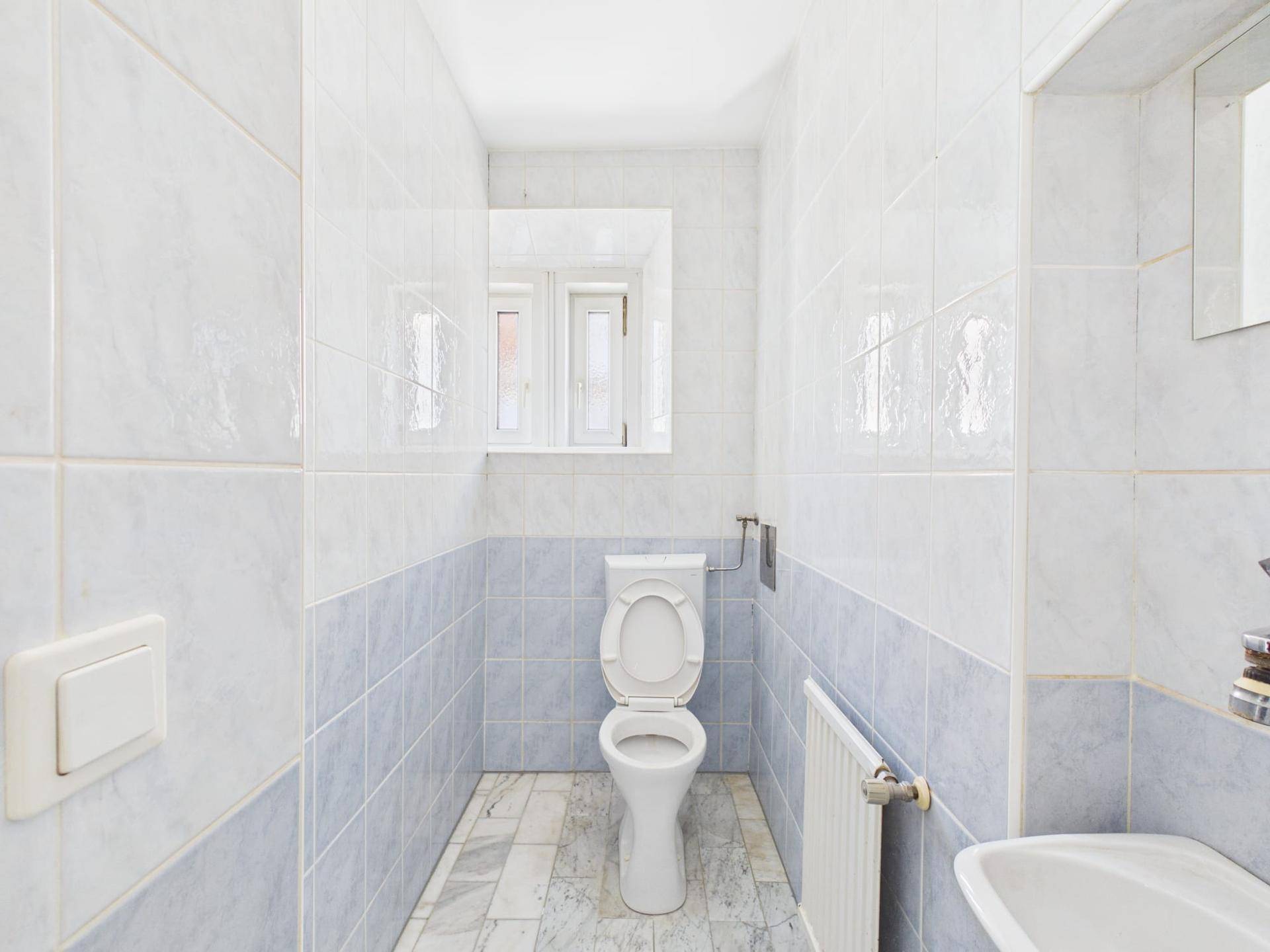 Modern gefliestes WC mit Toilette, Waschbecken und Heizkörper.