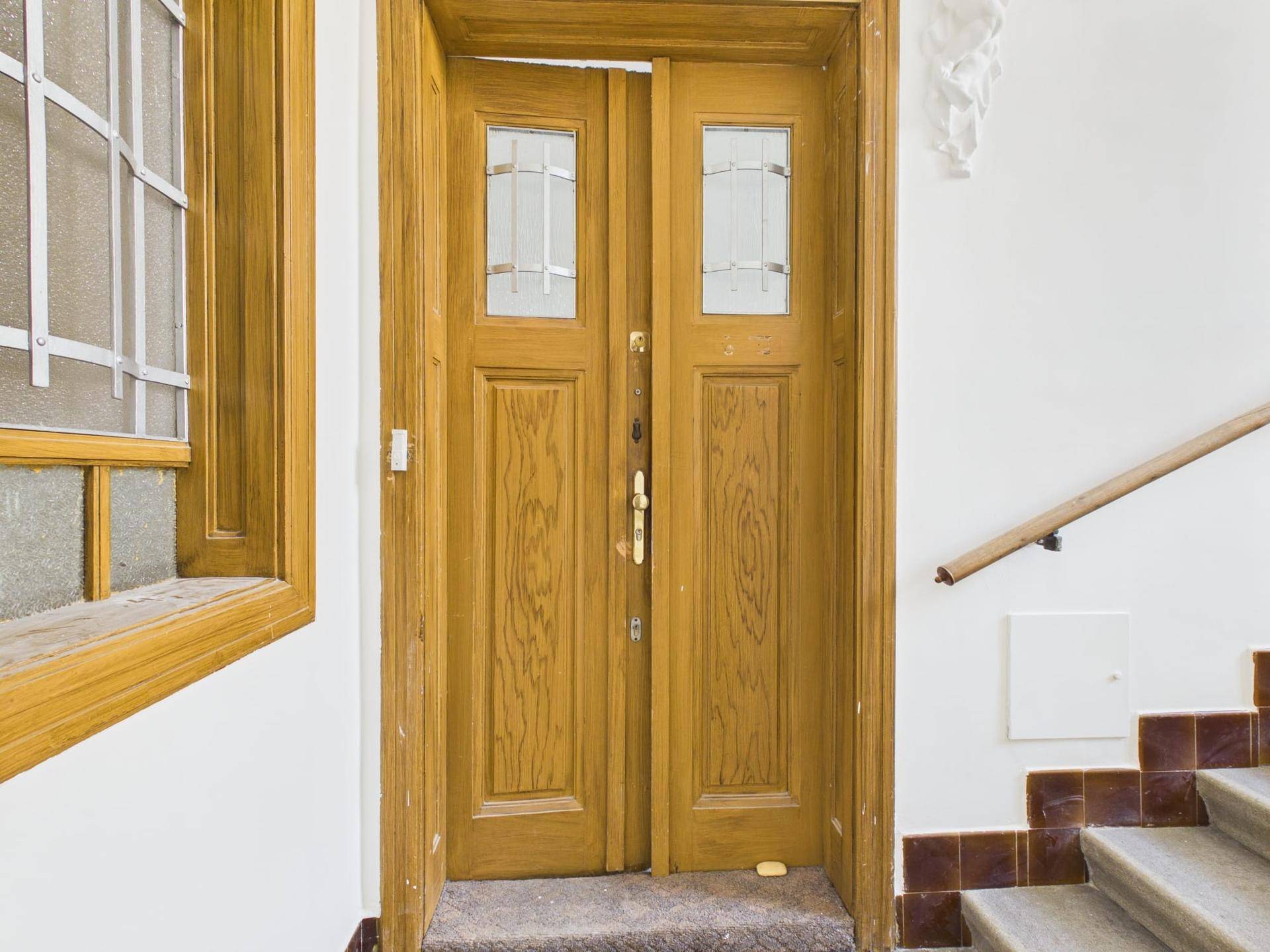 Eingangsbereich mit Holztür, Treppe und Fenster mit Gitter, typisch für Altbau.