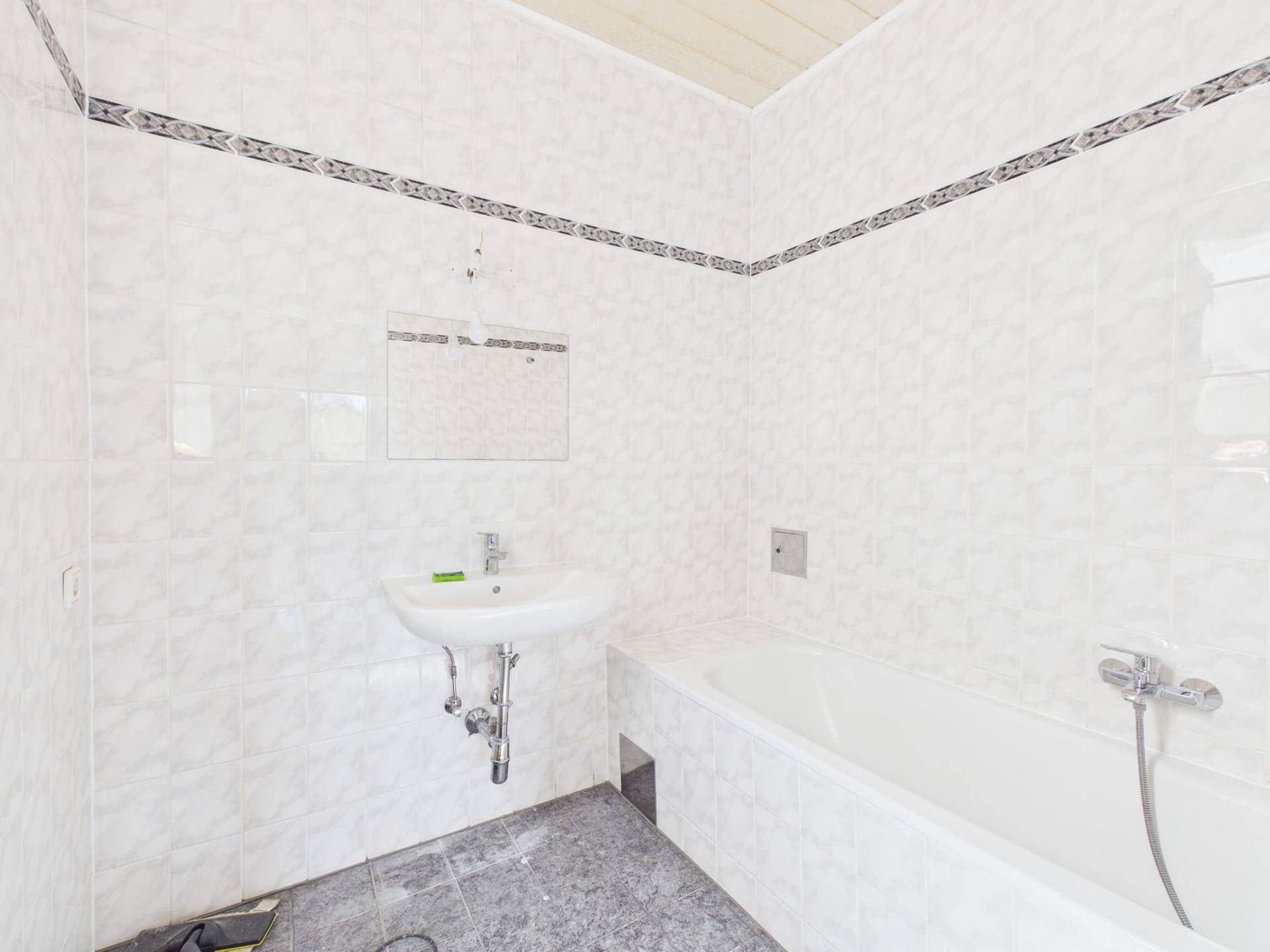Badezimmer mit weißen Fliesen, Badewanne mit Duschfunktion und Waschbecken.