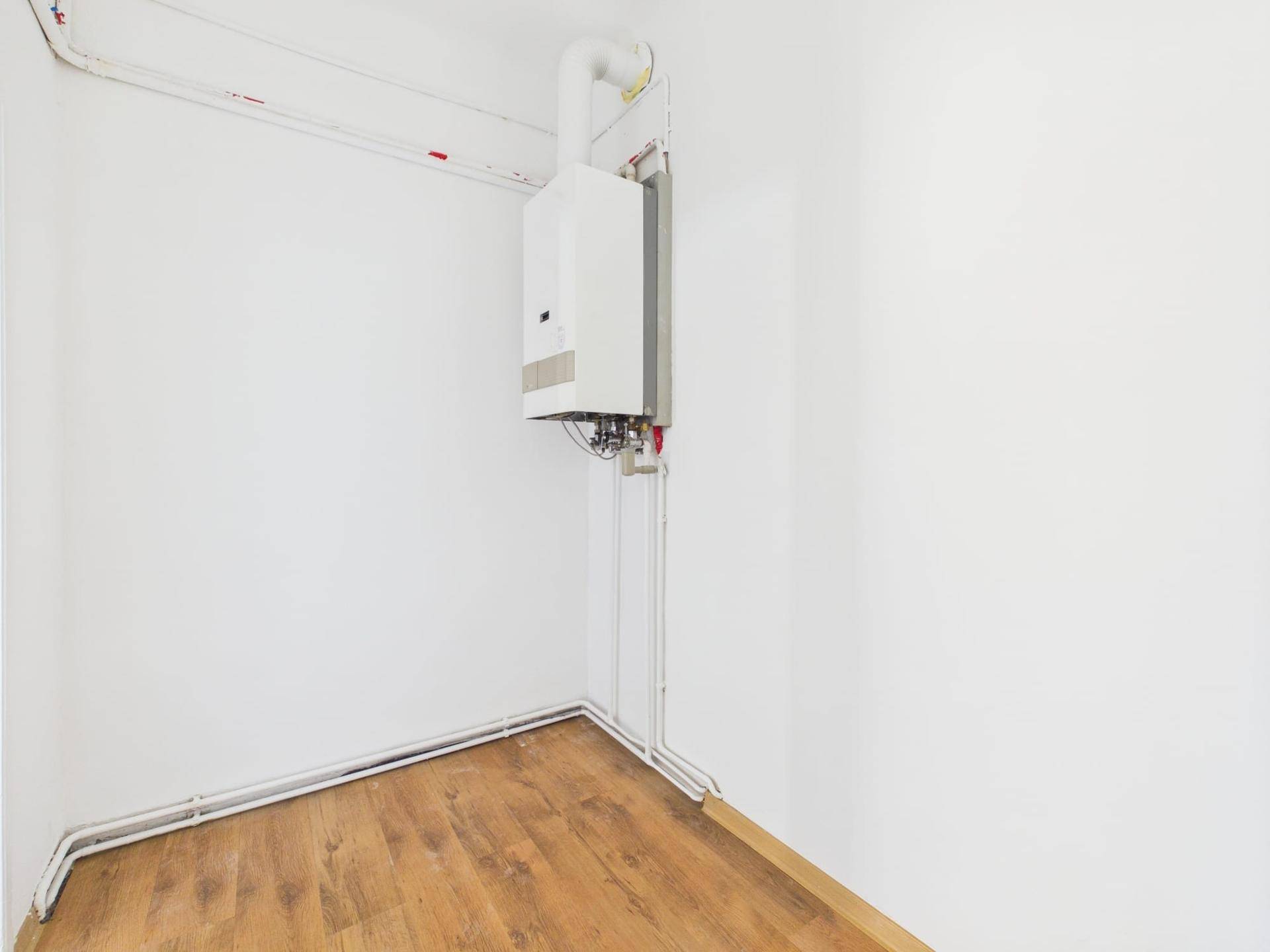 Kleiner Abstellraum mit Gastherme und sichtbaren Leitungen an den weißen Wänden.