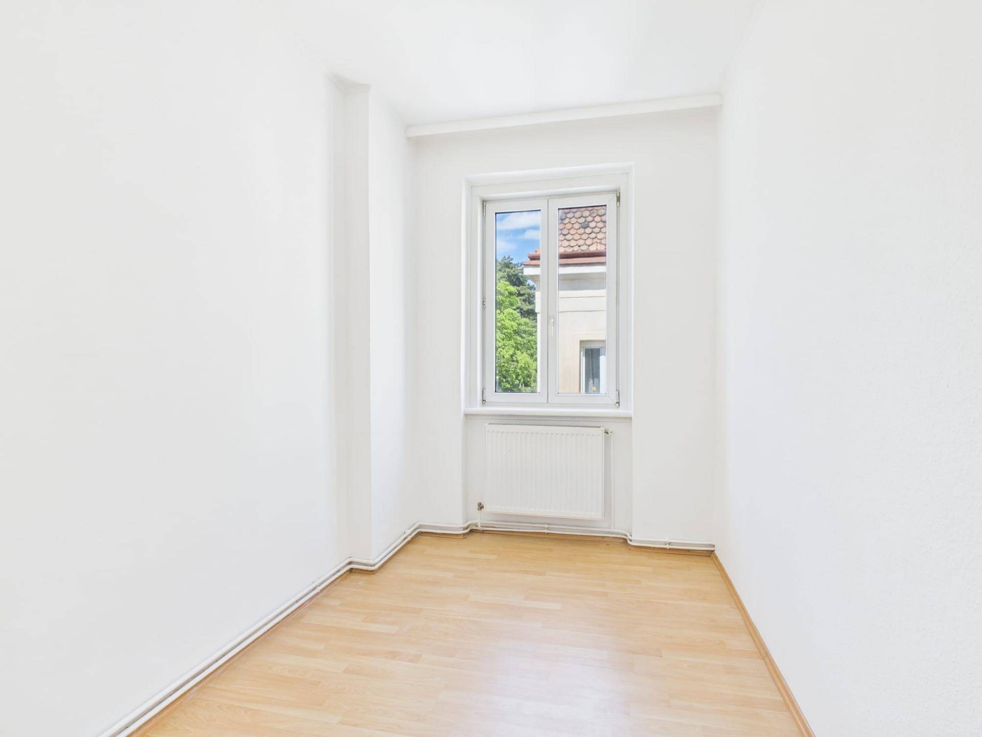 Kleiner, heller Raum mit Laminatboden, weißen Wänden und Fensterblick auf die Umgebung.
