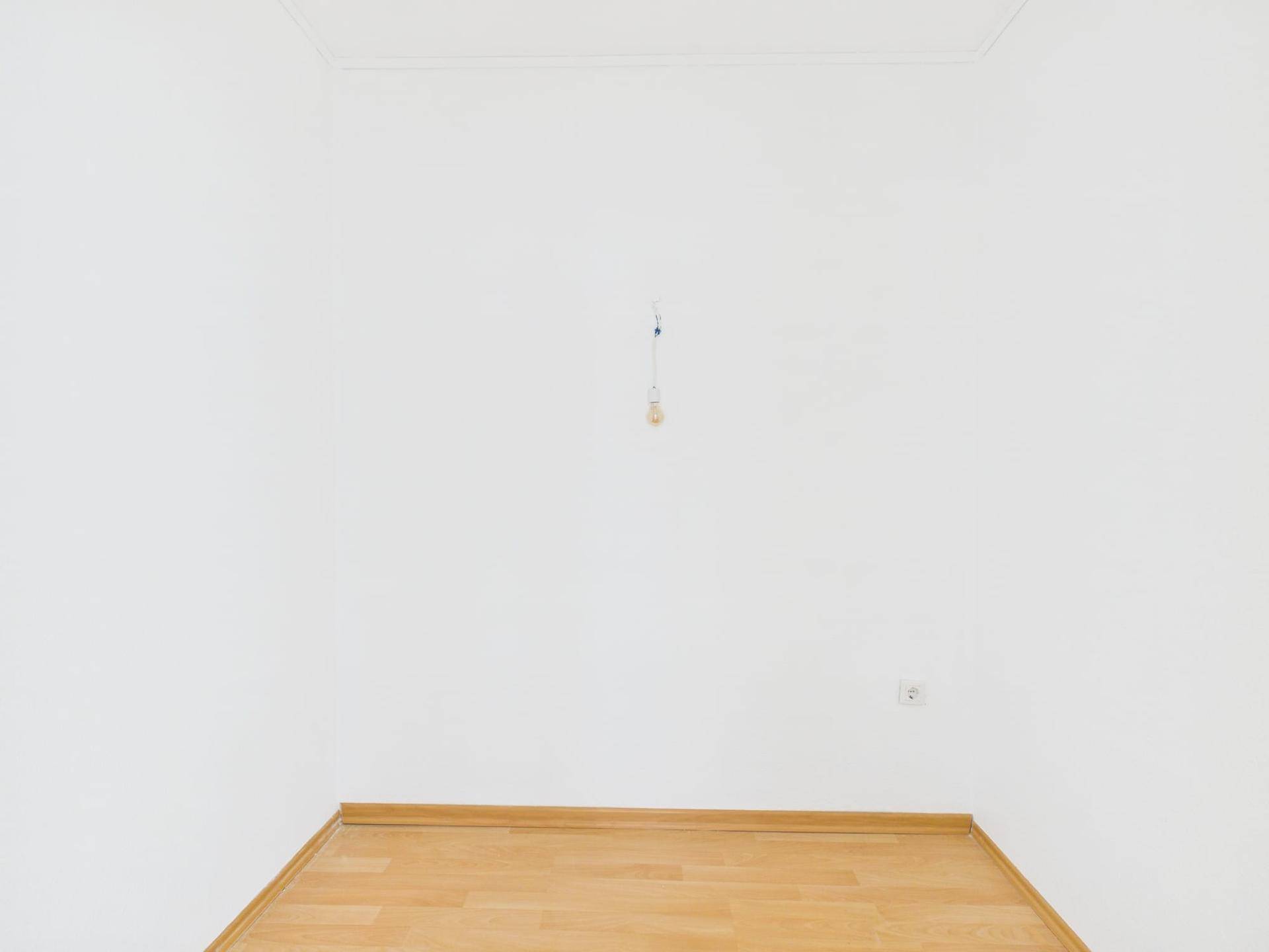 Schlichter, leerer Raum mit weißen Wänden und hellem Laminatboden, bereit zur Einrichtung.