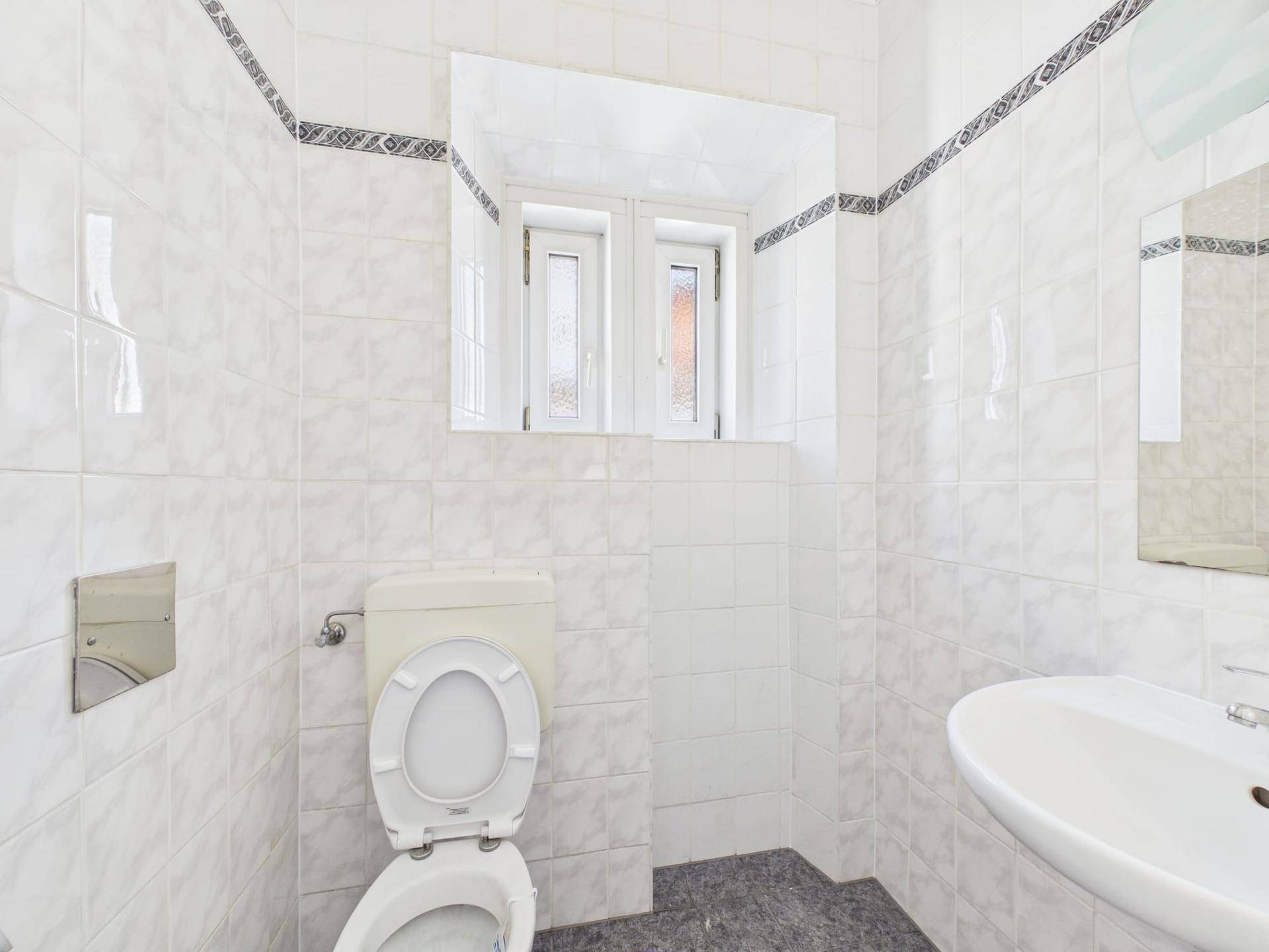 WC mit weißen Fliesen, Toilette, Waschbecken und Fenster mit Milchglas.