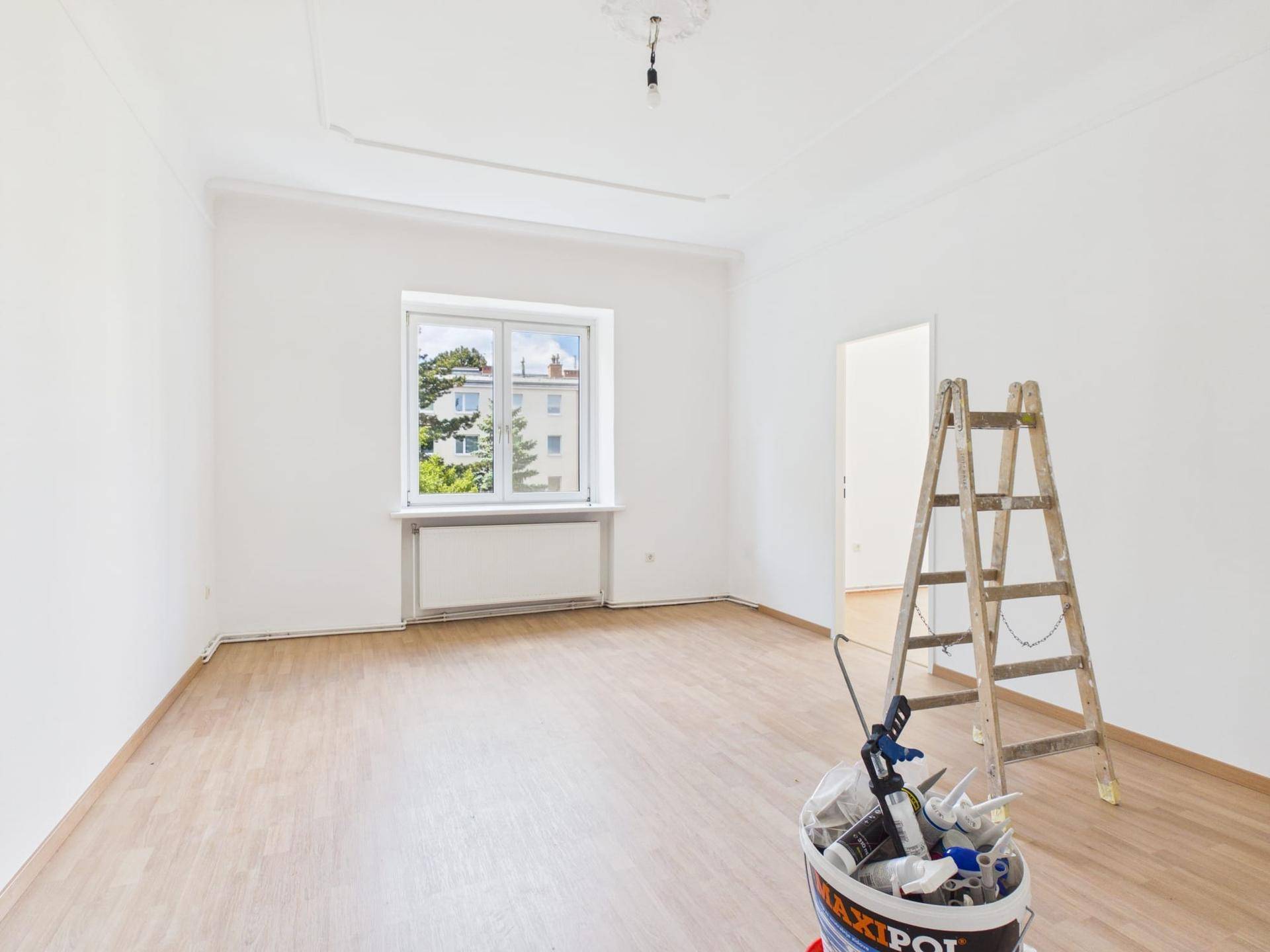 Heller Wohnraum mit Laminatboden, weißen Wänden und Ausblick ins Grüne sowie auf Nachbargebäude.