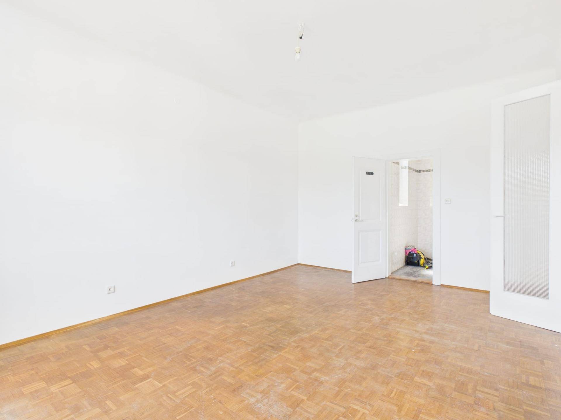 Geräumiger Wohnraum mit Parkettboden und Zugang zu einem gefliesten Bereich.