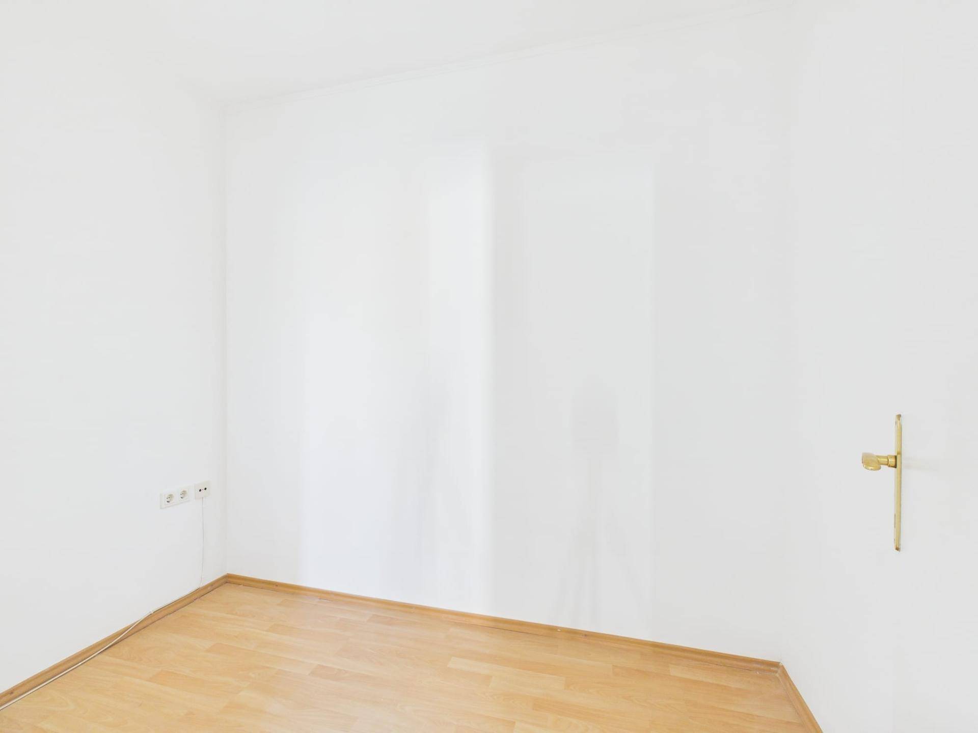 Leerer Raum mit weißen Wänden und hellem Laminatboden, bereit zur individuellen Gestaltung.
