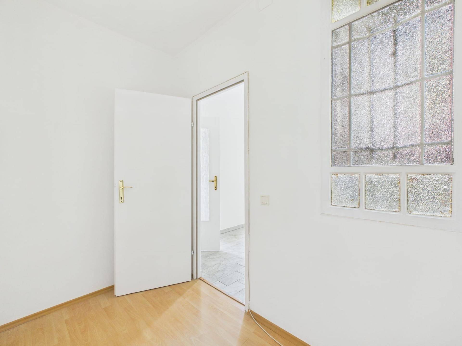 Heller Raum mit Laminatboden und einer Tür, die in einen weiteren Bereich führt, mit Fenster.