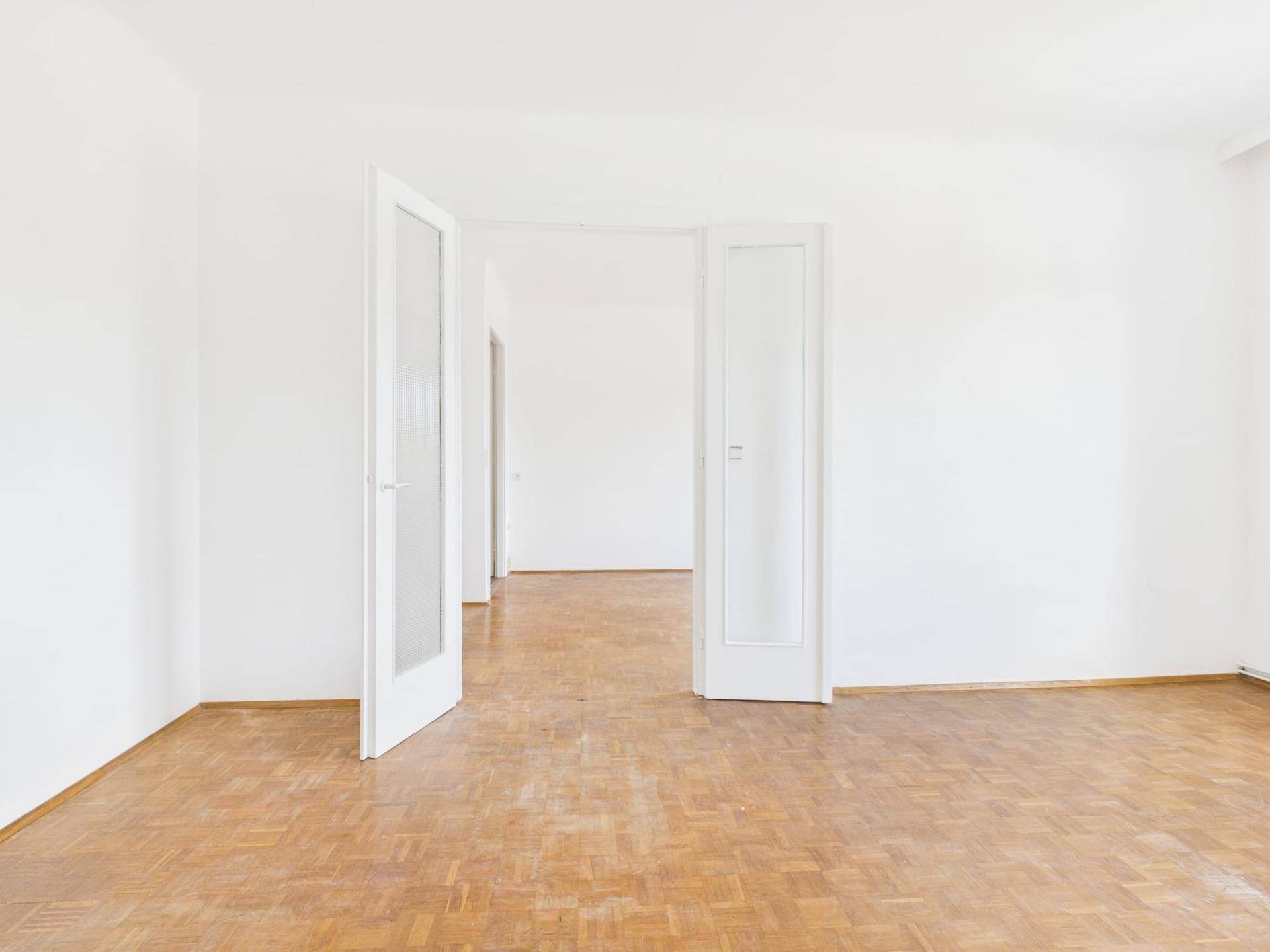 Heller Wohnraum mit Parkettboden und offenen Türen, die eine großzügige Raumverbindung schaffen.