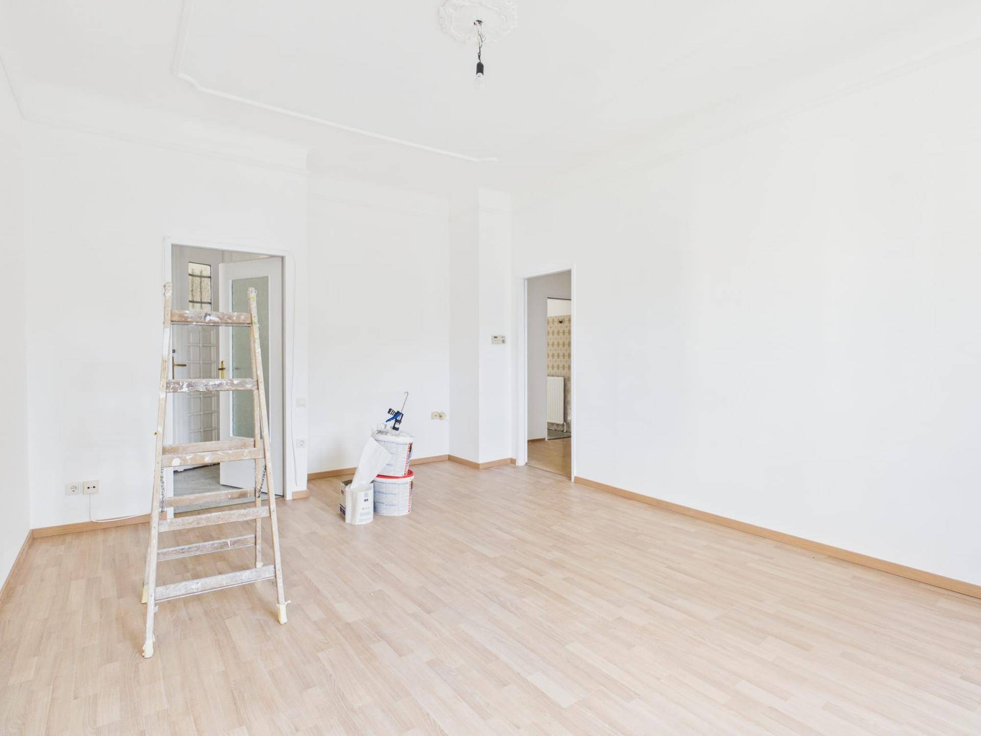 Geräumiger, heller Wohnbereich mit Laminatboden, weißen Wänden und Renovierungsbedarf.