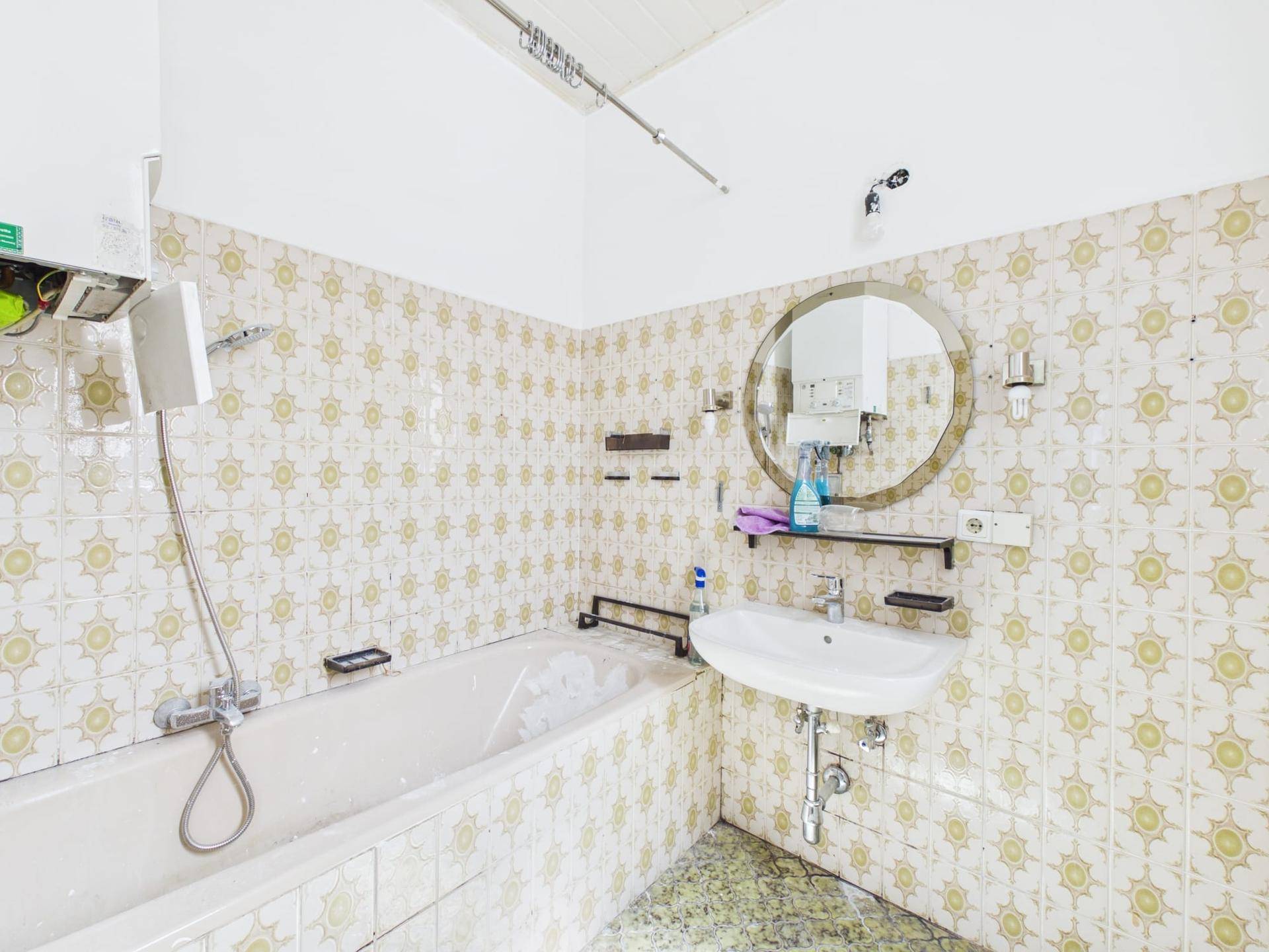 Badezimmer mit gelb-weiß gemusterten Fliesen, Badewanne und Waschbecken mit rundem Spiegel.