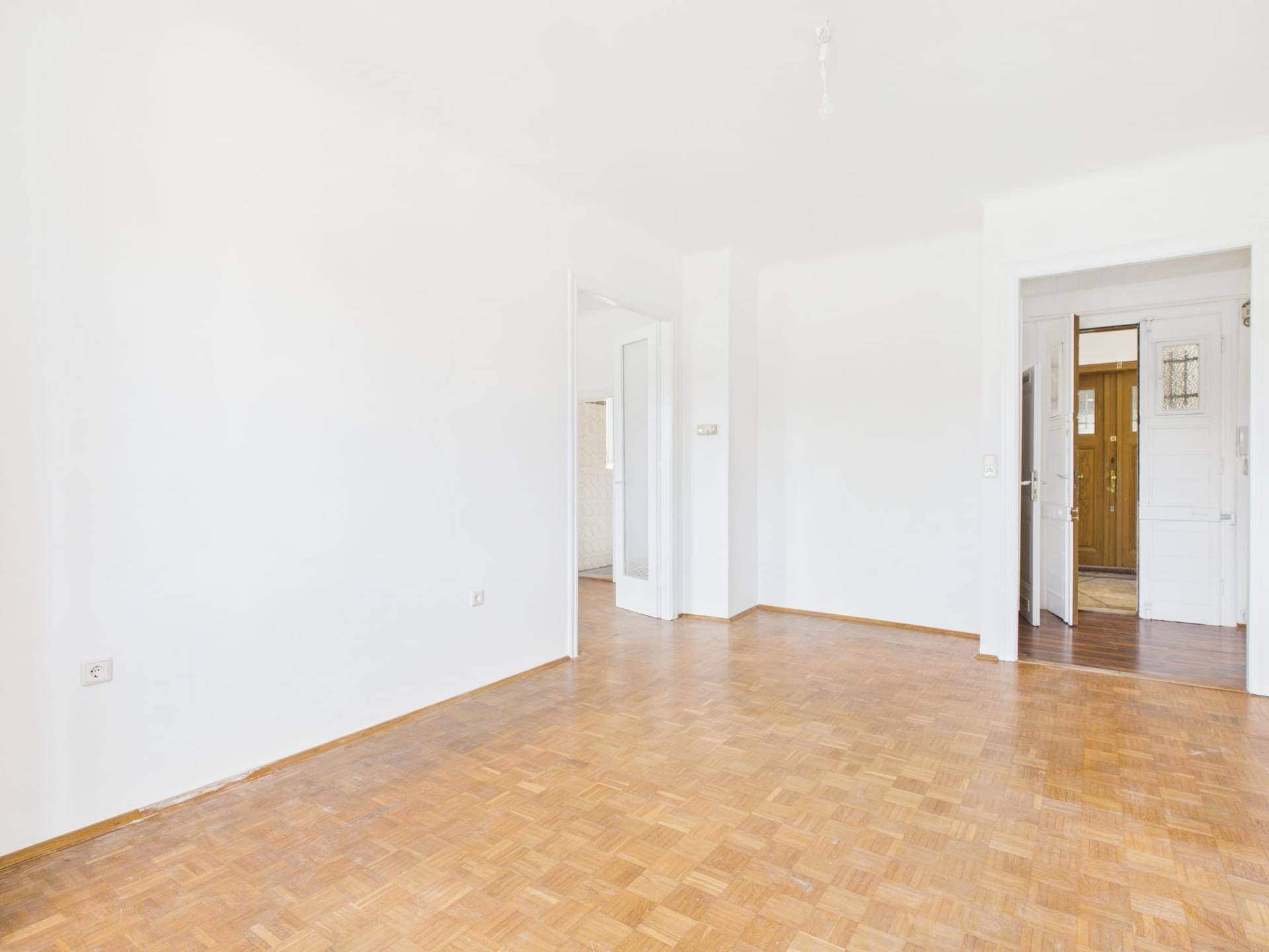 Geräumiges Zimmer mit hellem Parkettboden und Zugang zu weiteren Räumen der Wohnung.