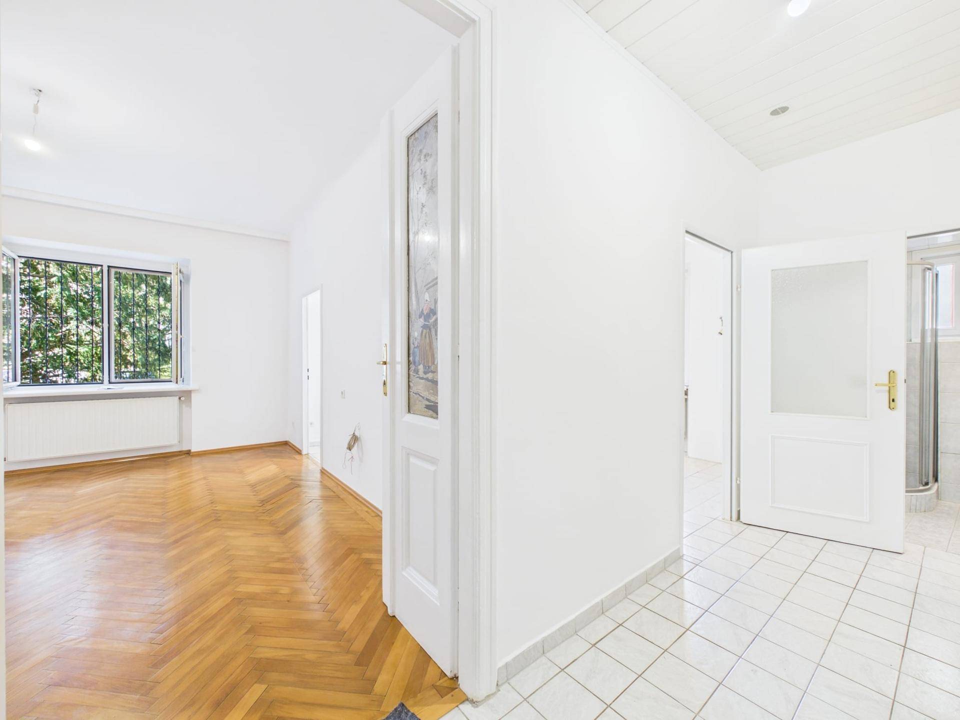 Heller Flur mit Fliesenboden, der zu einem Wohnzimmer mit Parkett führt.