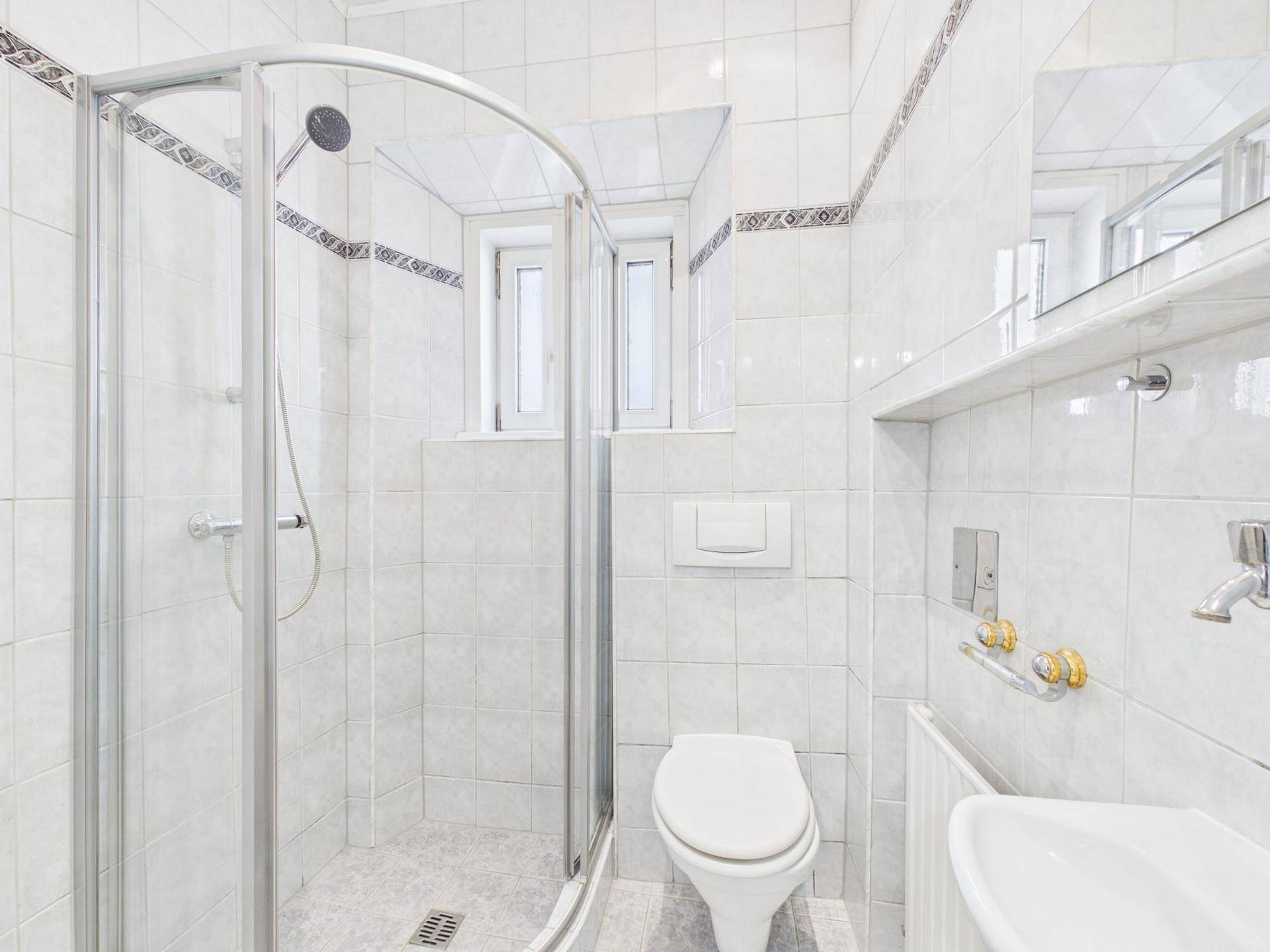 Helles Badezimmer mit Duschkabine, WC und Waschbecken, komplett gefliest.