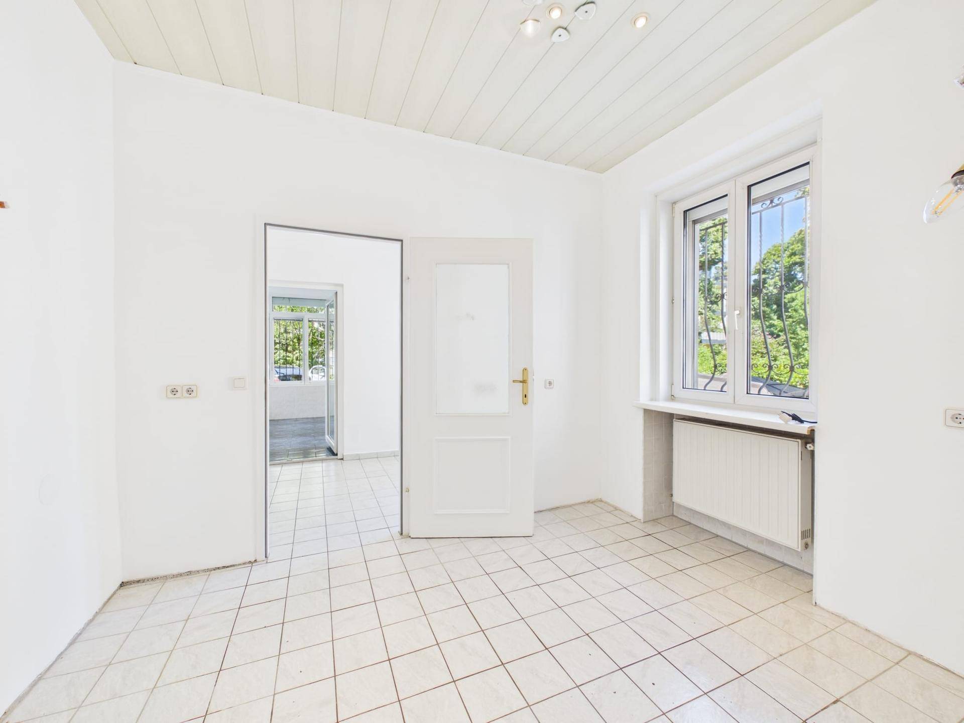 Leerer Raum mit Fliesenboden und Fenster, der auf den Garten blickt.