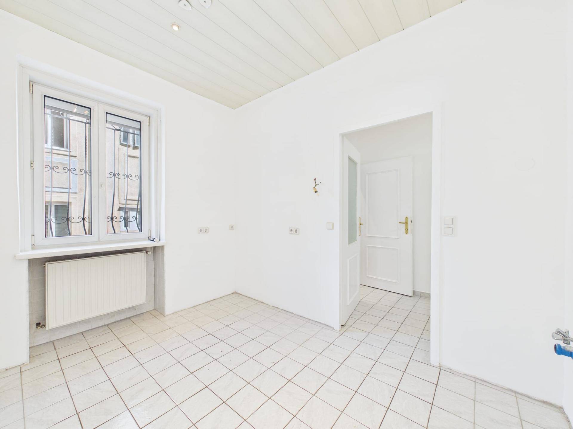 Leerer Raum mit Fliesenboden und Fenster, das auf die Straße blickt.