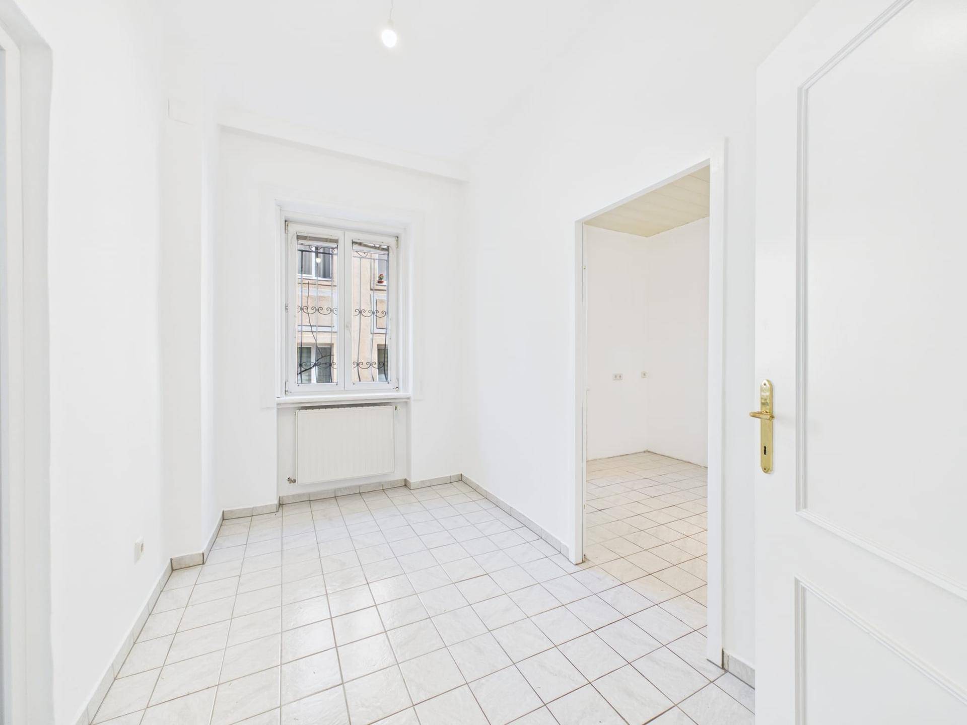 Leerer Raum mit Fliesenboden und Fenster, das auf die Straße blickt.