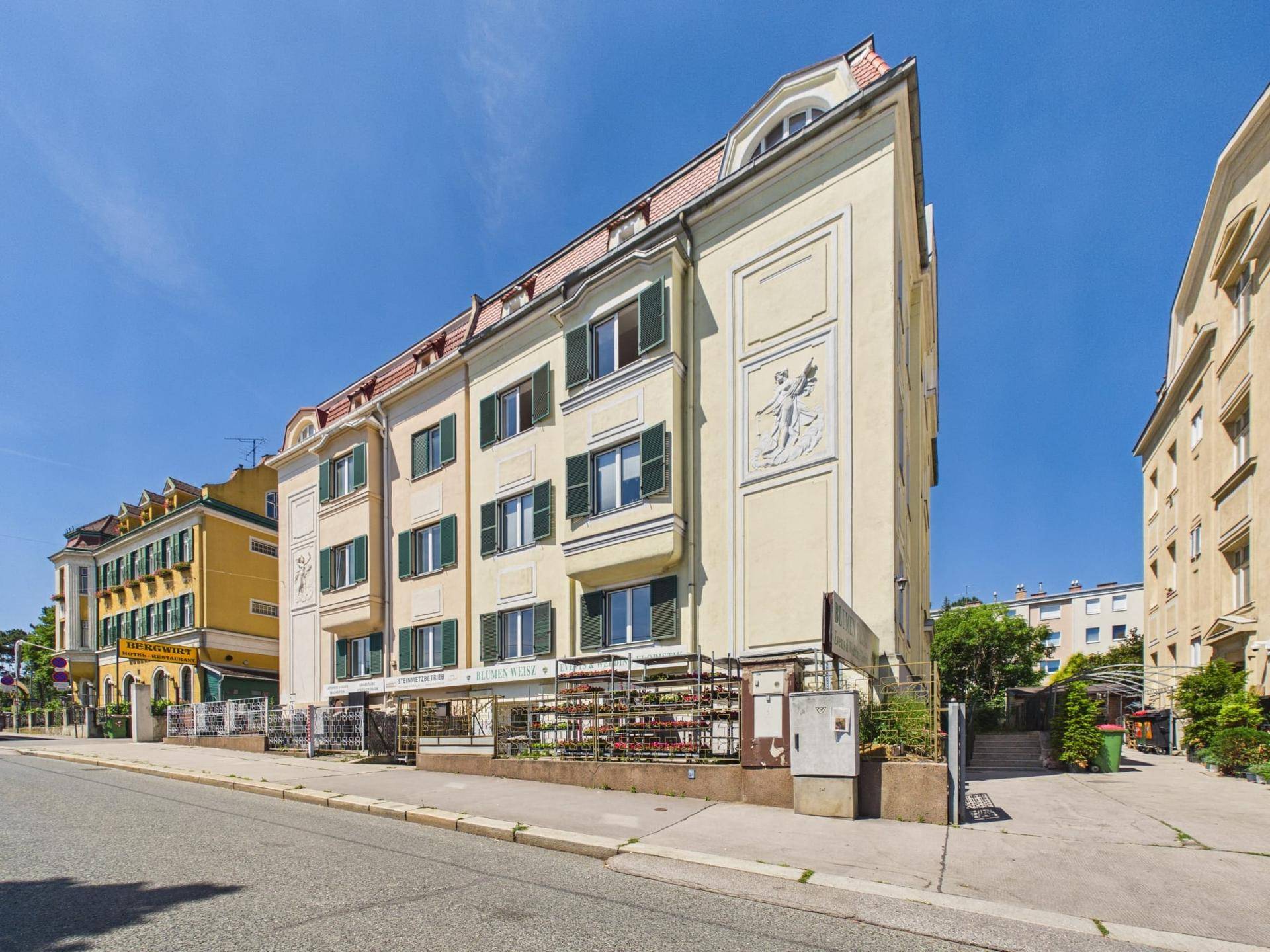 Historisches Gebäude mit klassischer Fassade, grünen Fensterläden und Mansarddach an einer Straße.