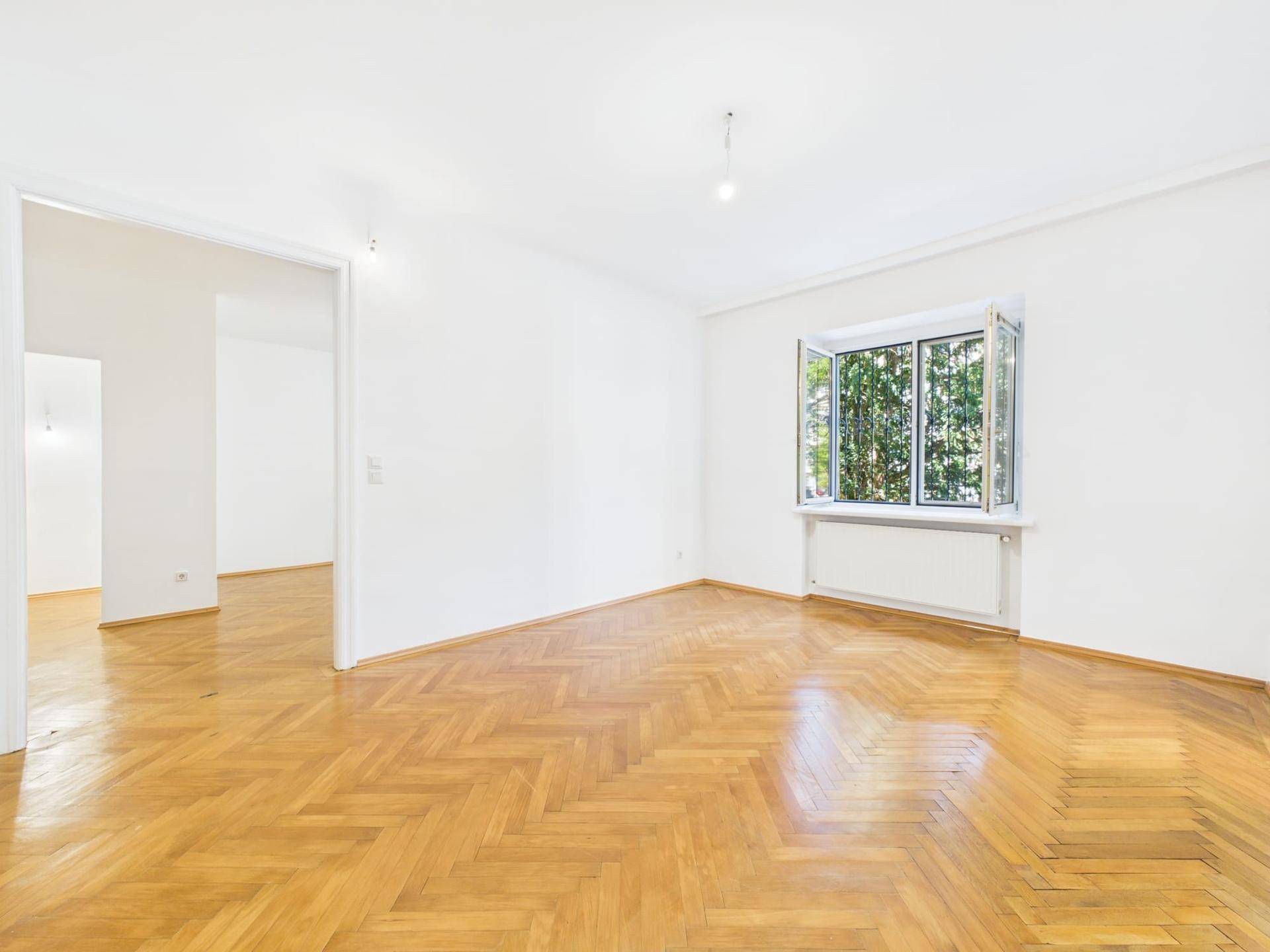 Helles Wohnzimmer mit Fischgrätparkett und Blick ins Grüne durch das Fenster.