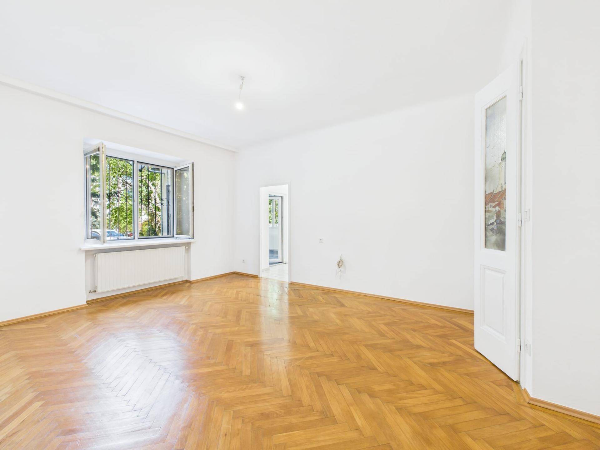 Geräumiges Wohnzimmer mit Fischgrätparkett und viel Tageslicht.