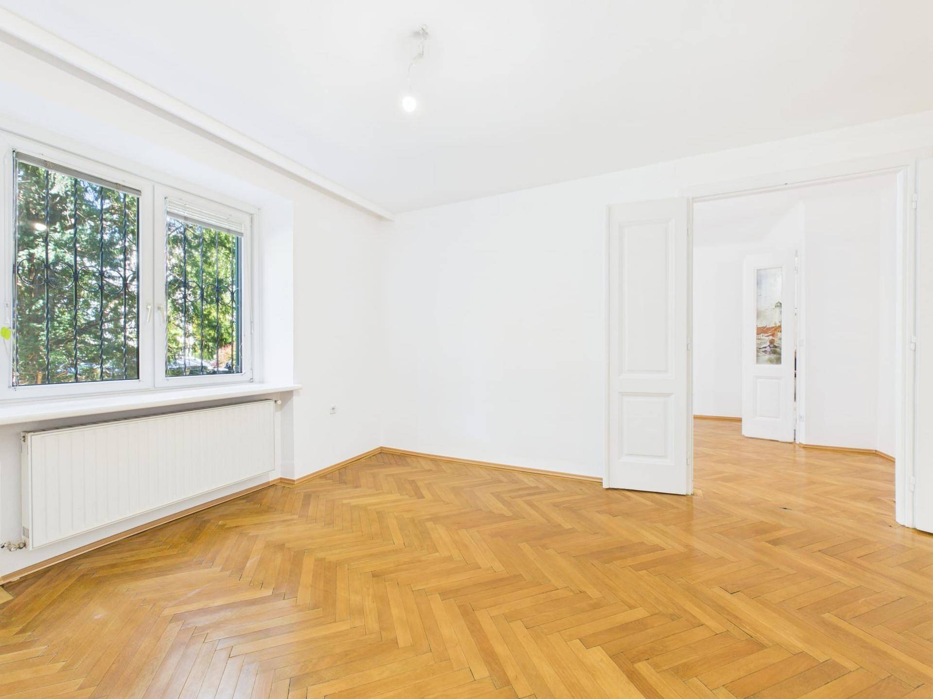 Großes Wohnzimmer mit Fischgrätparkett, weißen Wänden und Blick ins Grüne.