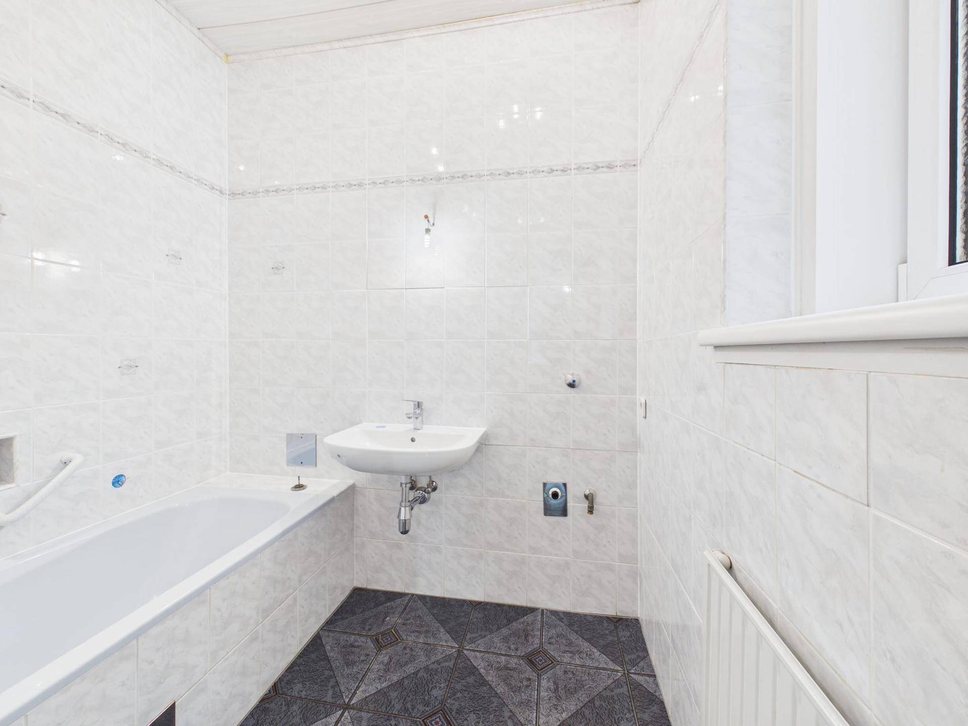Helles Badezimmer mit Badewanne, Waschbecken und Fliesenboden.