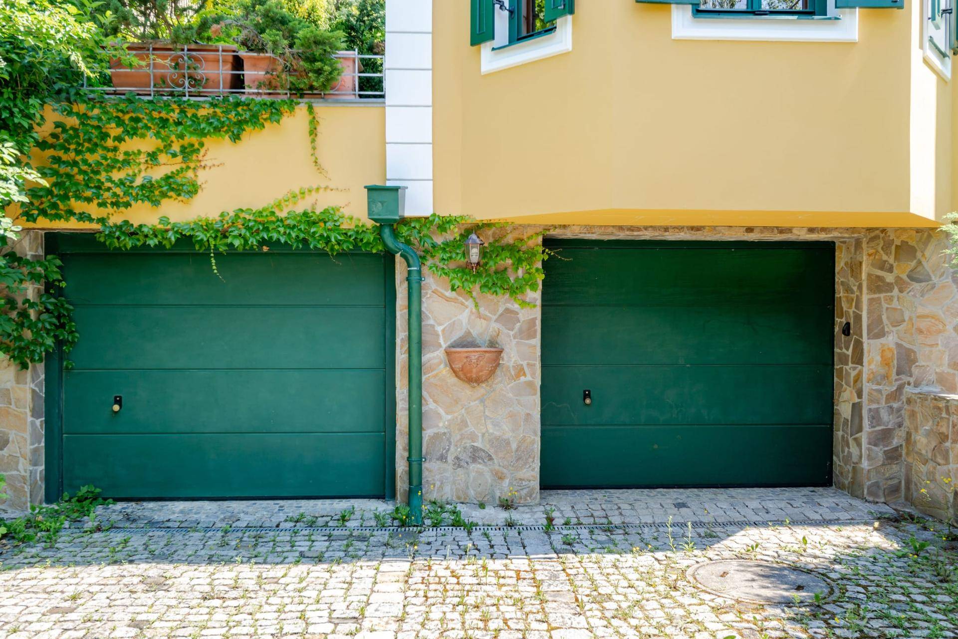 Geschlossene Doppelgarage mit grünen Toren und Steinverkleidung, umgeben von Efeu.