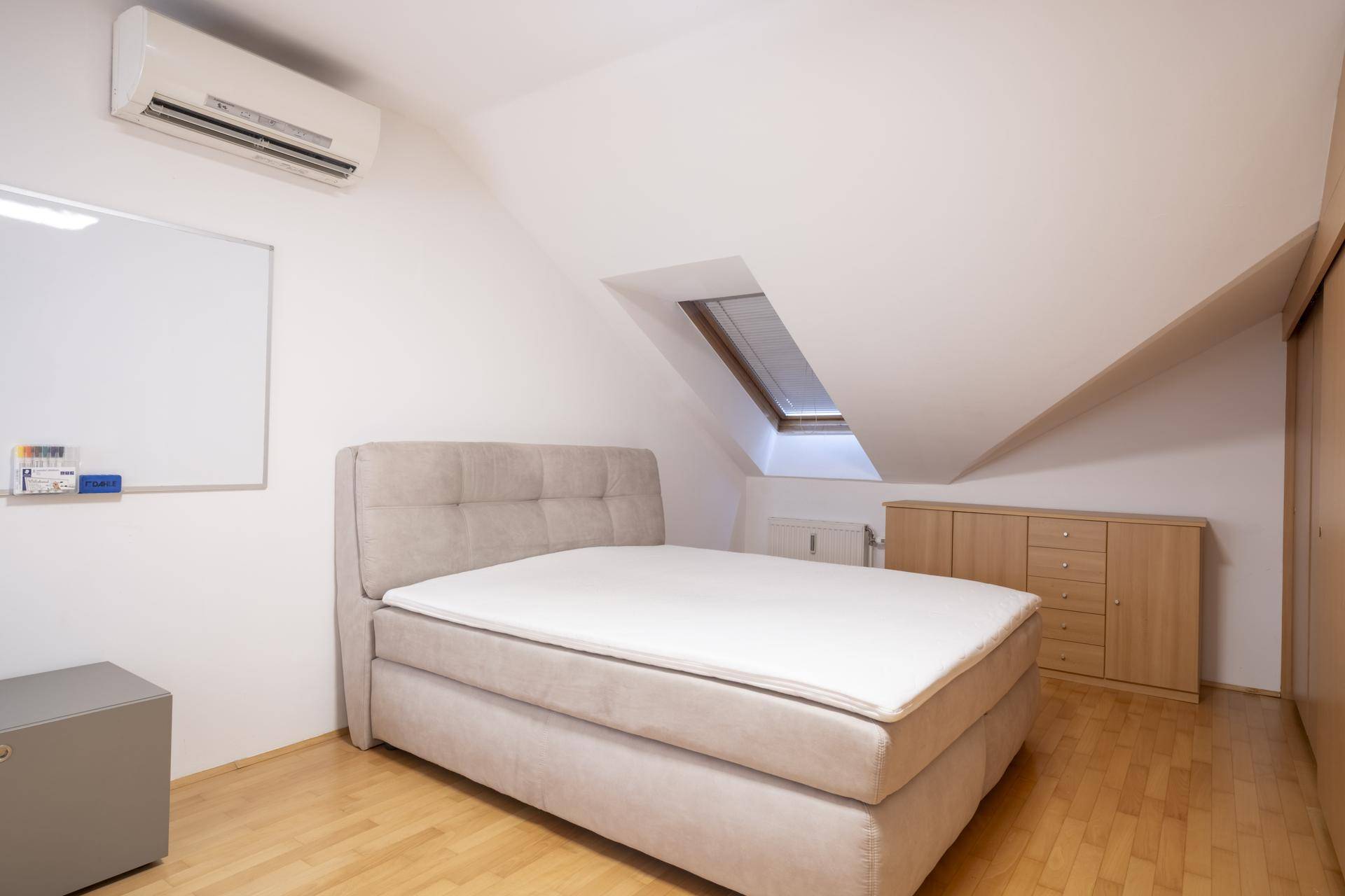 Helles Schlafzimmer im Dachgeschoss mit Bett, Klimaanlage und Dachfenster.