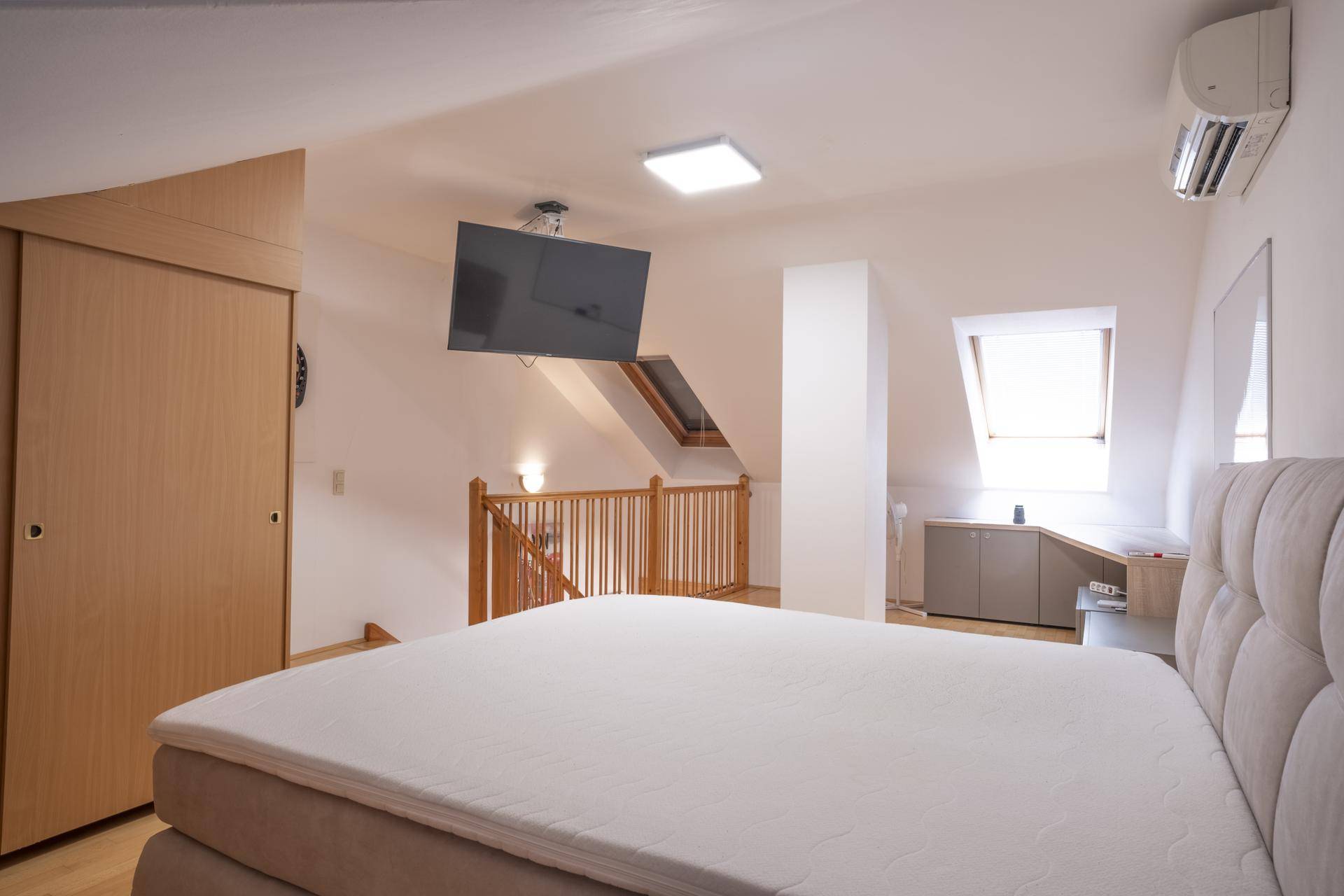 Schlafzimmer im Dachgeschoss mit Bett, Einbauschränken und Blick auf die offene Treppe.