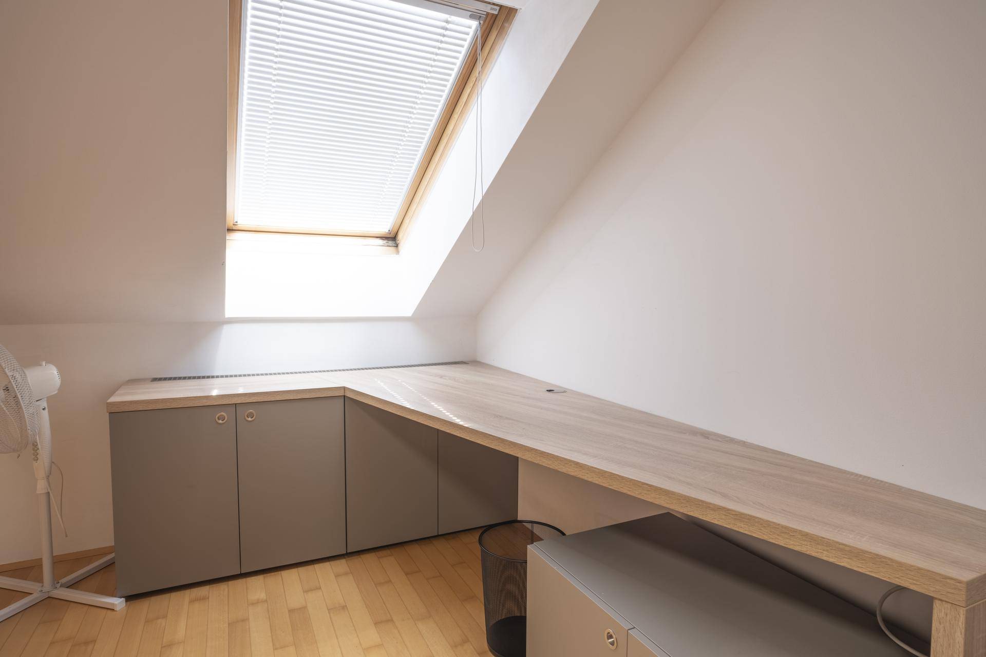 Heller Arbeitsbereich im Dachgeschoss mit großem Schreibtisch, Stauraum und Dachfenster.