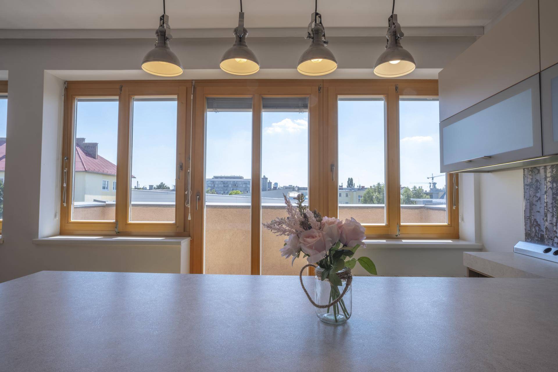 Helle Küche mit Kücheninsel, Hängelampen und weitem Stadtblick durch große Fenster.