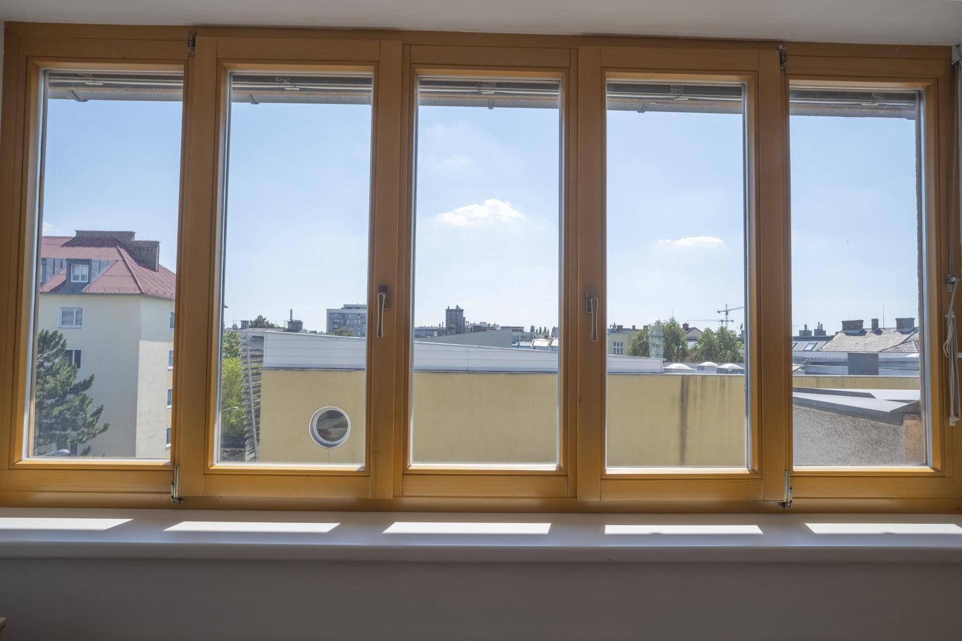 Große Holzfensterfront mit weitem Blick auf die umliegenden Gebäude und den blauen Himmel.