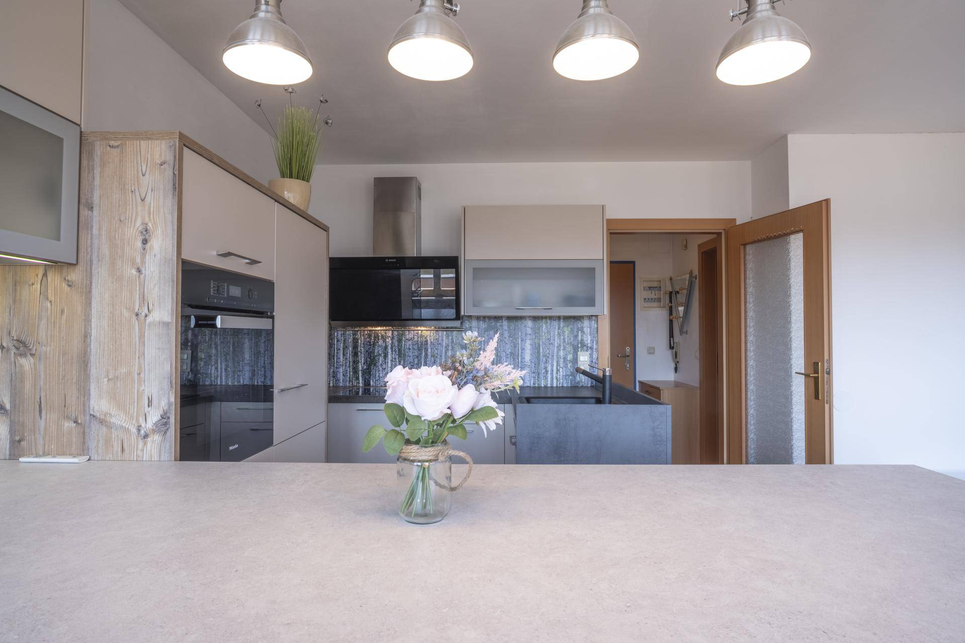 Moderne Küche mit Kücheninsel, integrierten Geräten und Blumenstrauß auf der Arbeitsplatte.