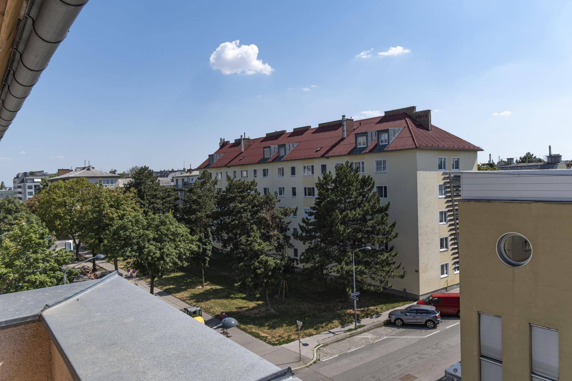 Blick von oben auf ein Wohngebäude mit rotem Dach, umgeben von Bäumen und weiteren Gebäuden.