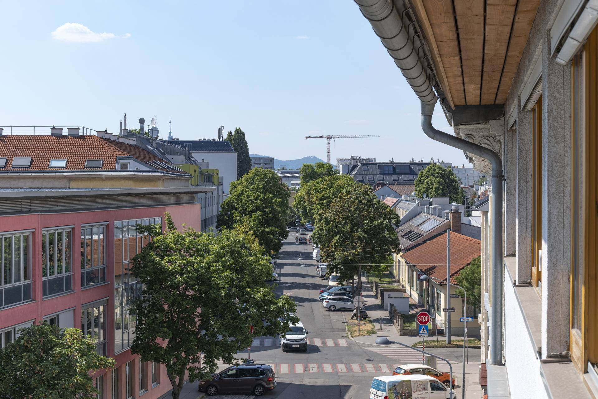 Panoramablick auf eine städtische Straße mit Gebäuden, Bäumen und Fahrzeugen unter blauem Himmel.