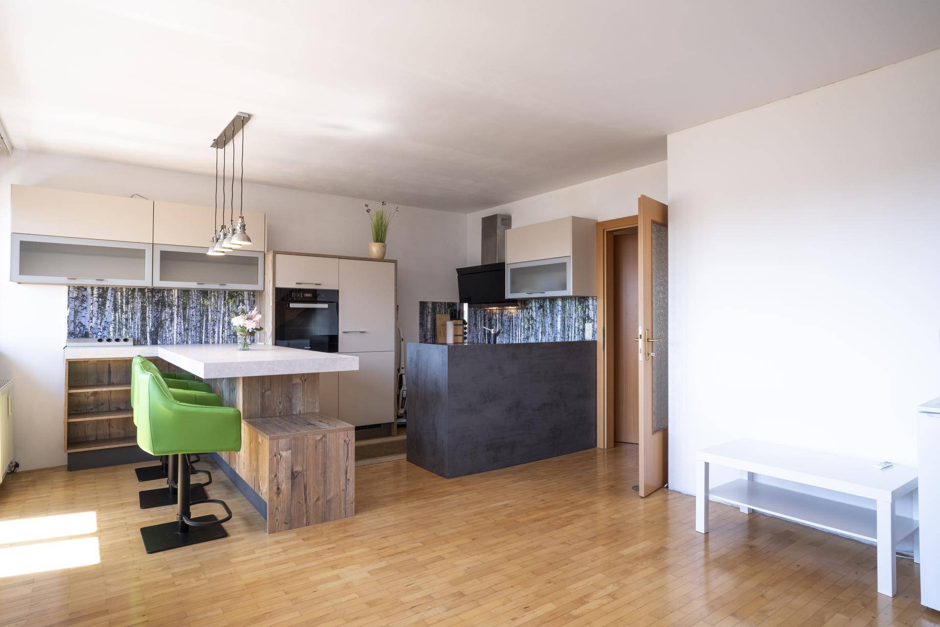 Moderne offene Küche mit Kücheninsel, Barhockern und Holzboden in einem hellen Wohnbereich.