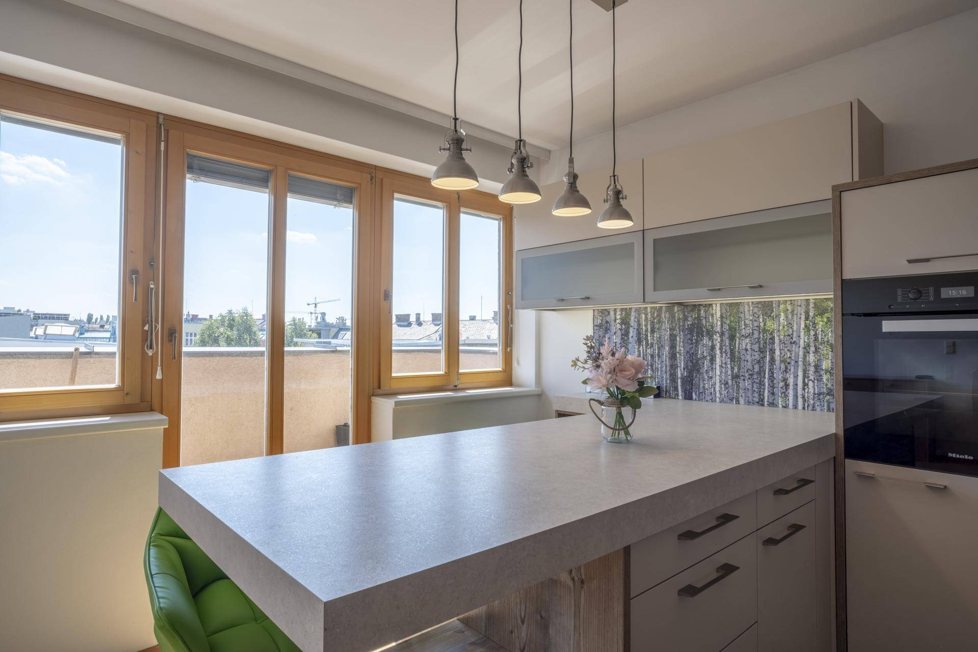 Moderne Küche mit Kücheninsel, Hängelampen und großen Fenstern mit Stadtblick.