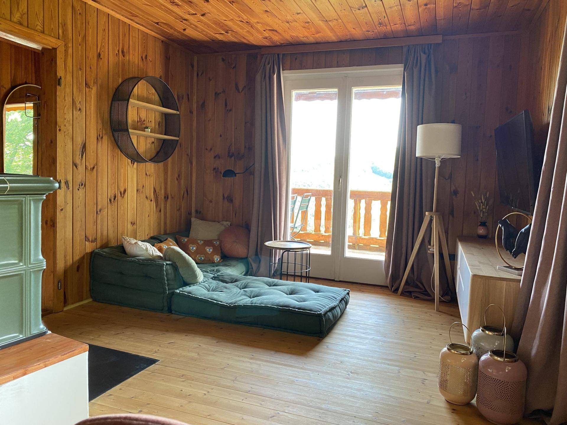 Gemütliches Wohnzimmer im alpinen Stil mit Holzvertäfelung und Zugang zum Balkon.