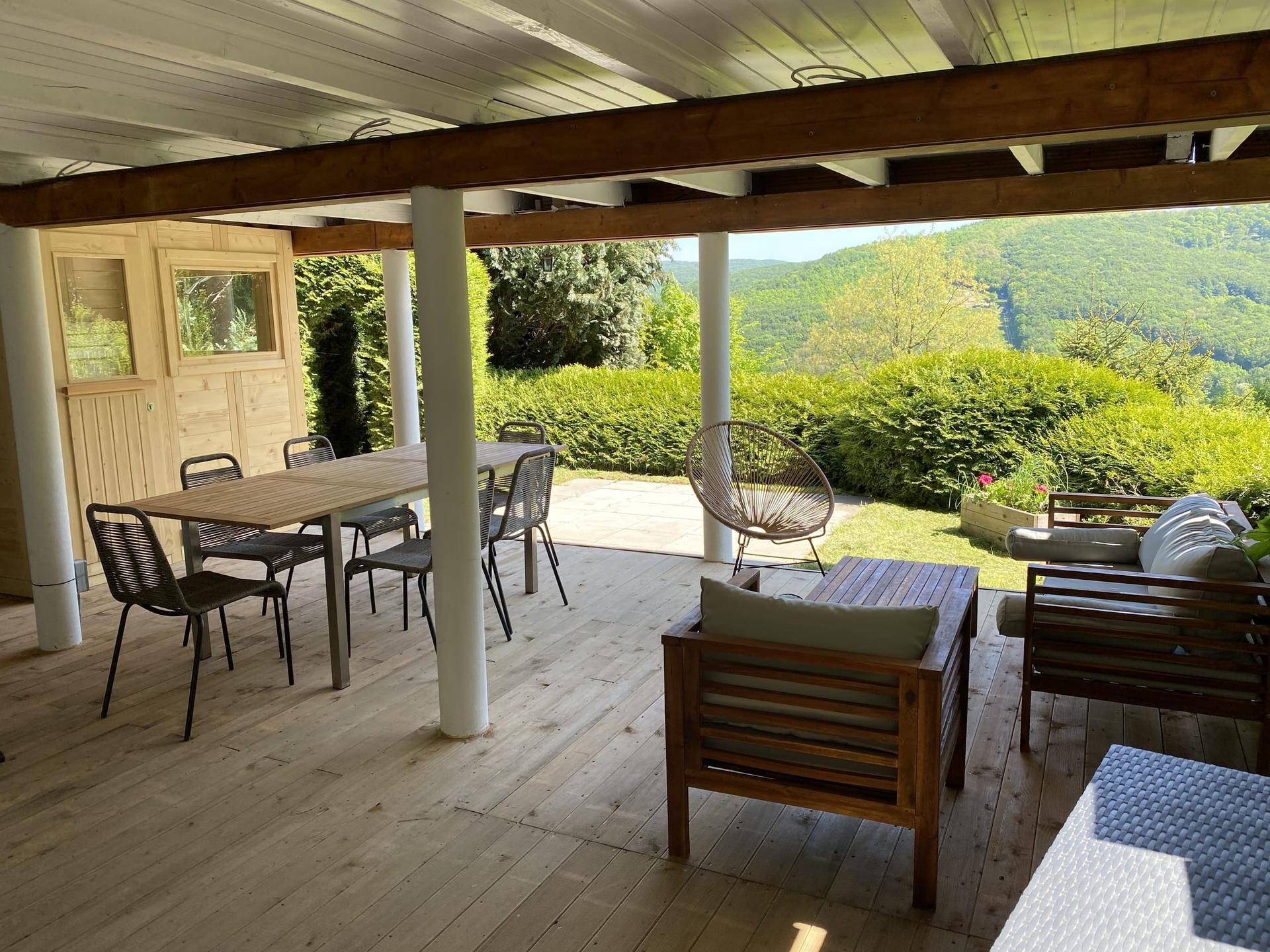 Überdachte Holzterrasse mit Ess- und Loungebereich, umgeben von viel Grün und Natur.